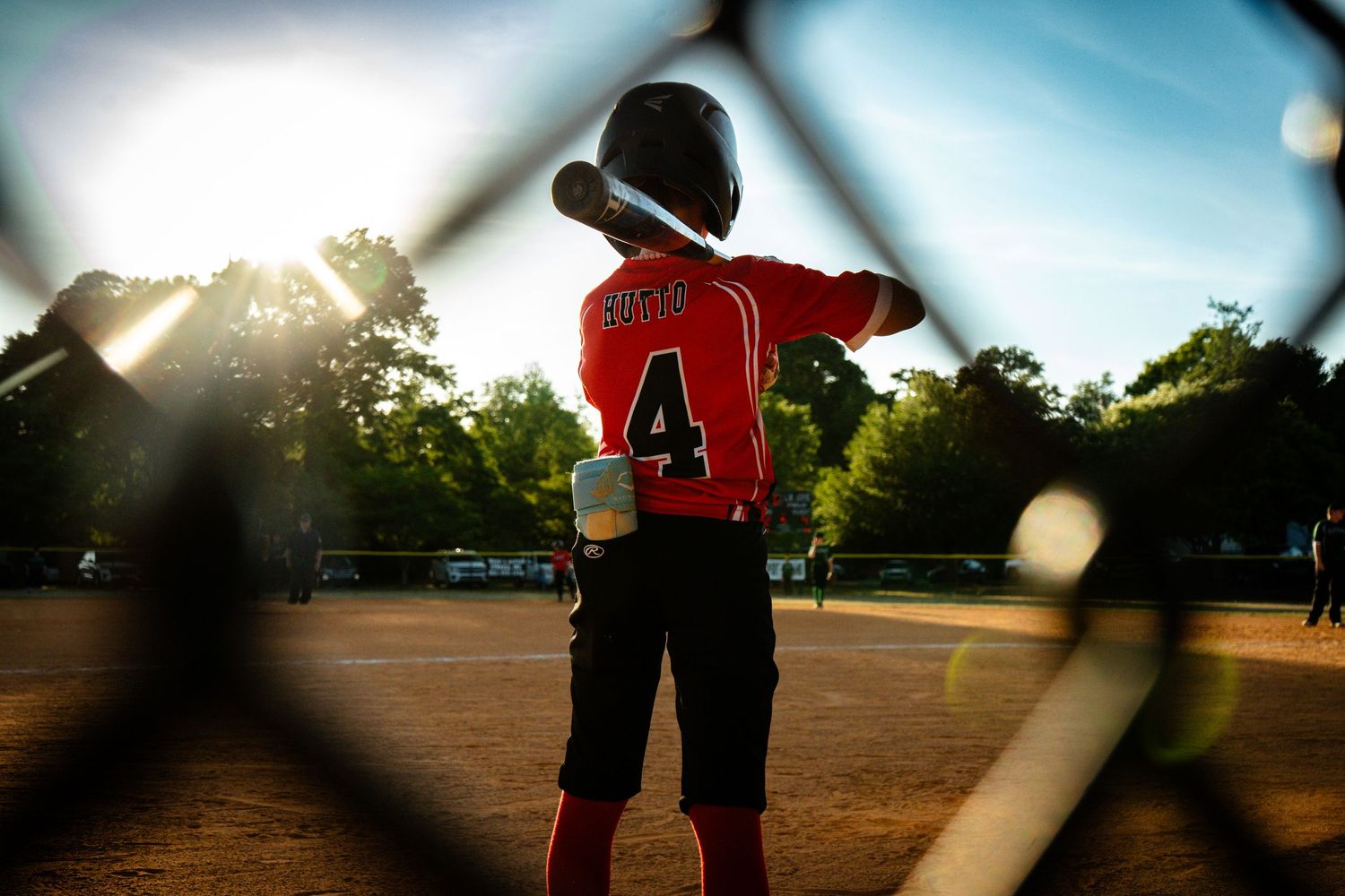 Young baseball player wearing number 4 jersey standing at bat on a sunlit field.