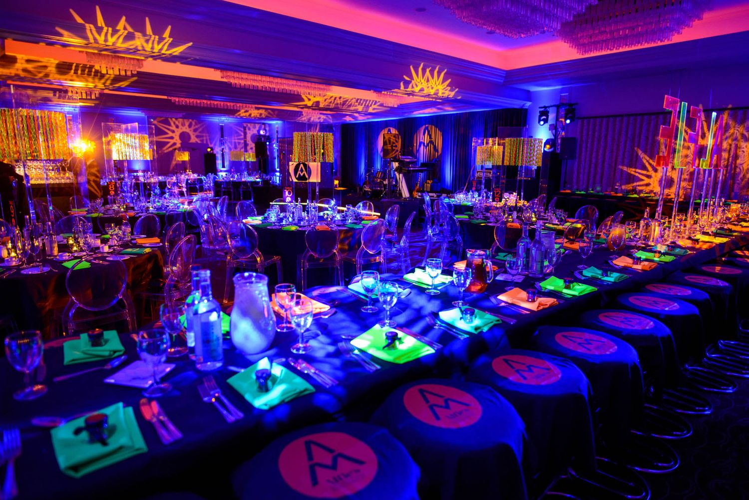 Elegant ballroom decorated with colorful LED lighting and ornate chandeliers featuring long dining tables set for a formal event.