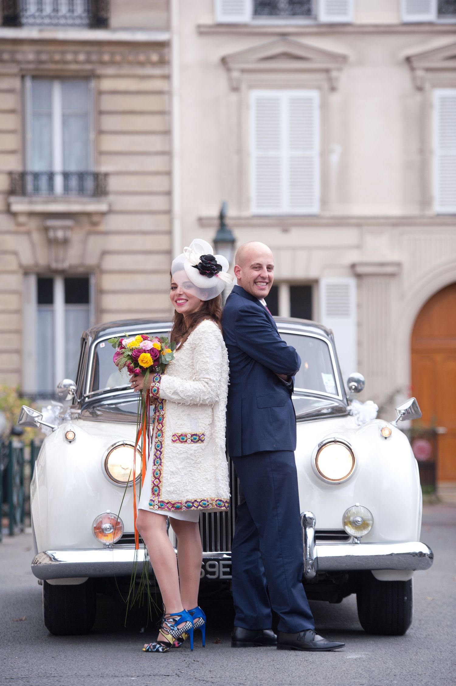 Vintage white classic car decorated with flowers and ribbons parked on a European city street for a wedding celebration.