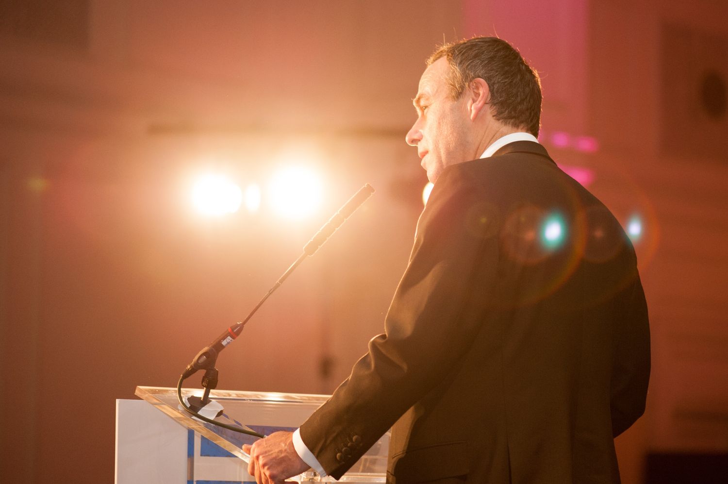 Silhouette of speaker at podium during presentation with dramatic lighting.