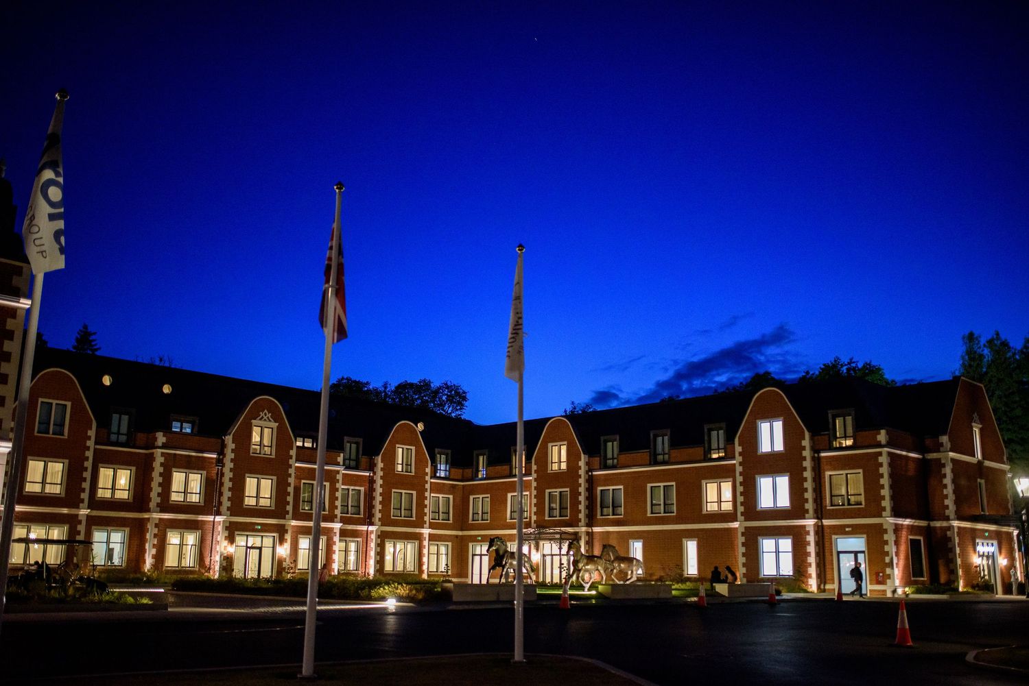 Historic brick buildings illuminated at night with glowing windows and dark blue sky create a dramatic architectural scene.
