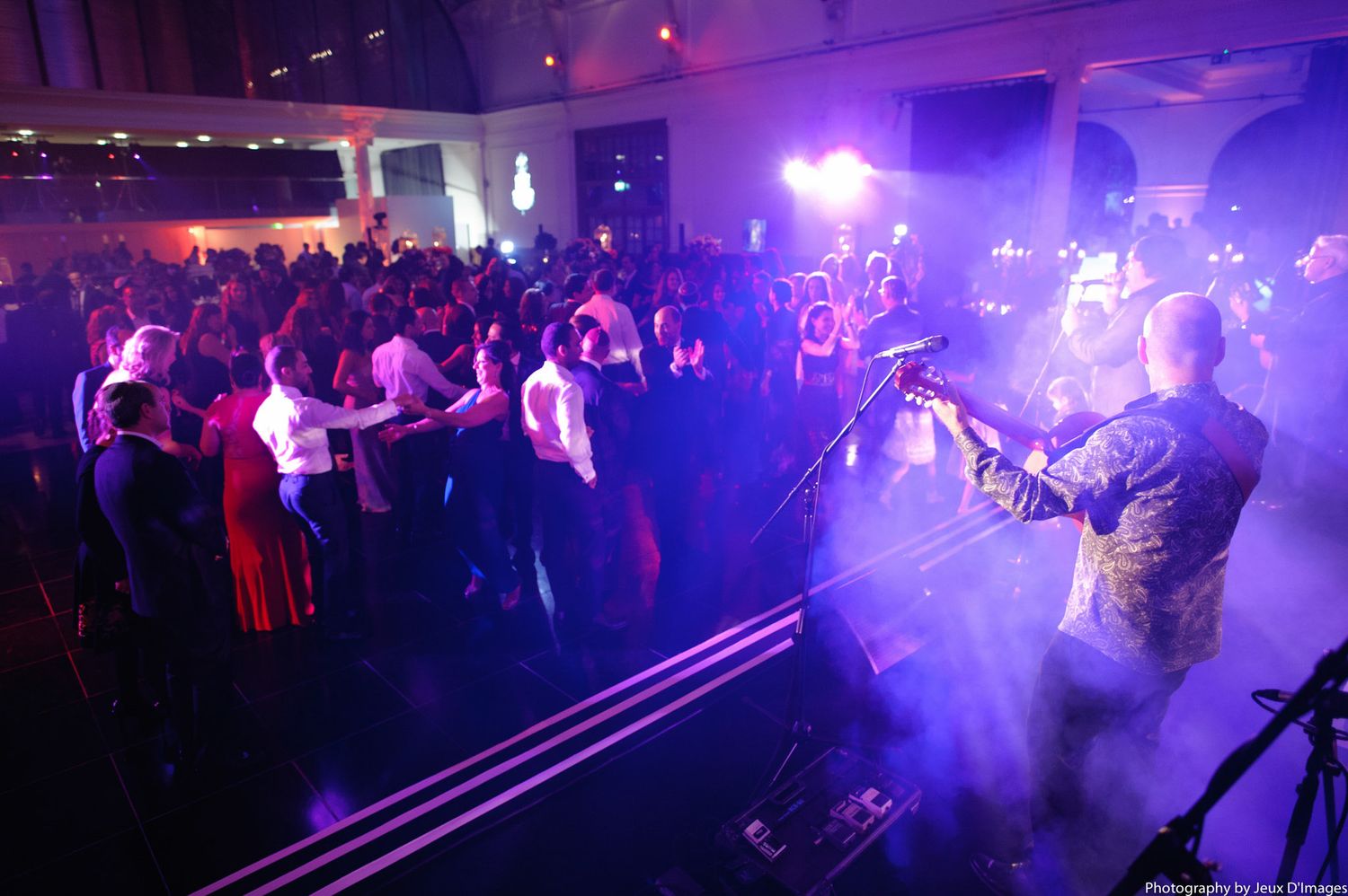 Dance floor filled with party-goers under dramatic purple stage lighting and fog effects.