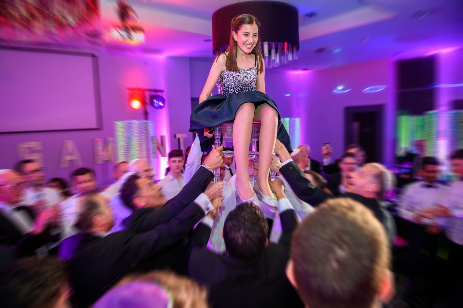 Crowd lifts and carries a person above their heads during a lively party with purple and blue lighting.