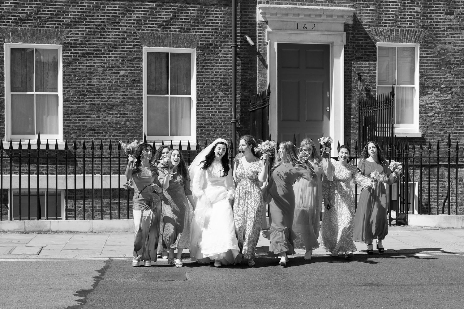 A black and white panoramic photograph shows a row of people standing in front of a brick building with windows.