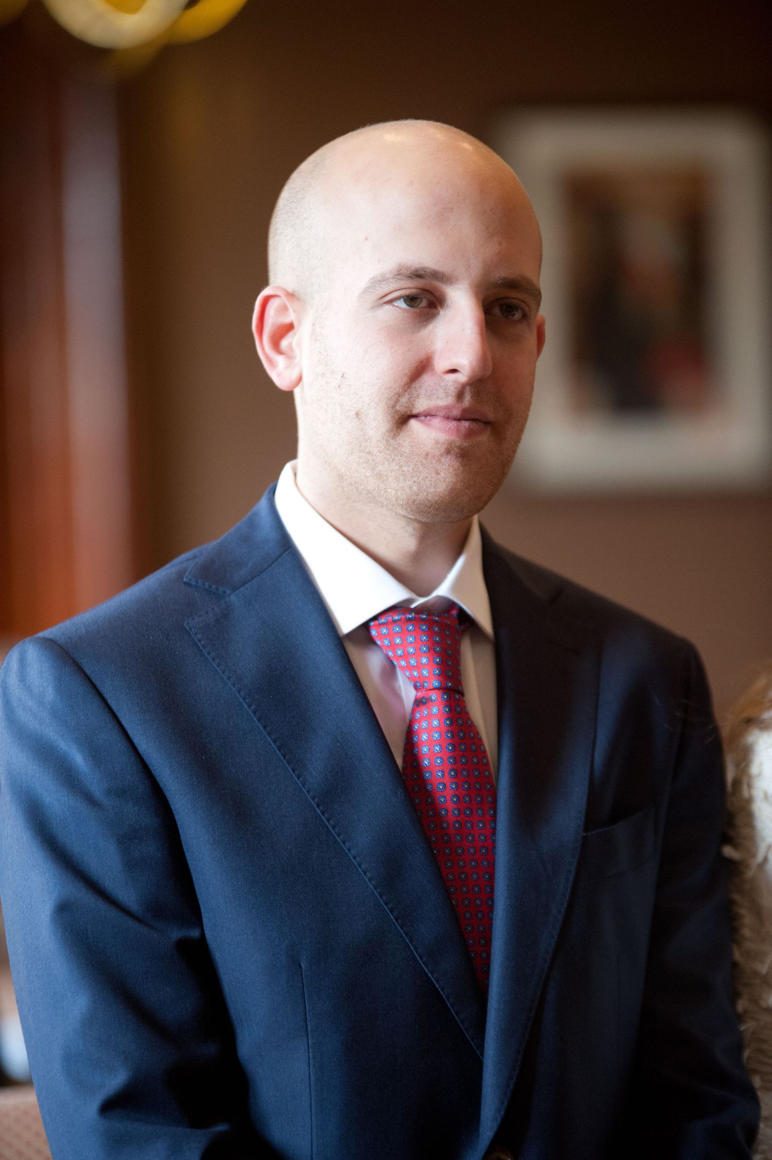 Professional portrait series showing a man in navy suit and red tie against a warm interior background.
