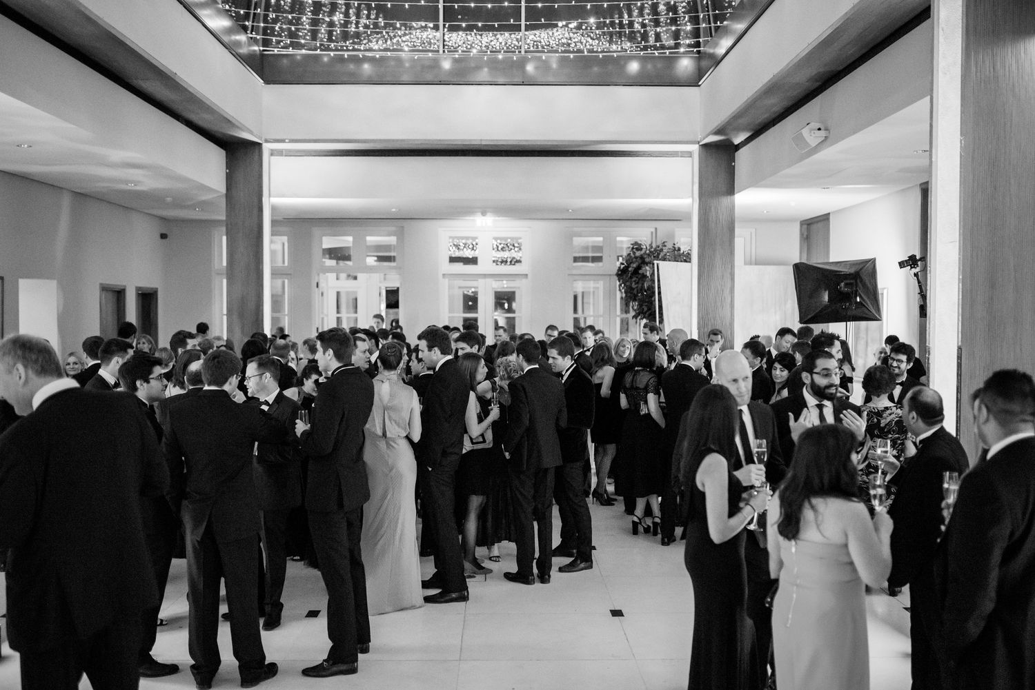 Wide angle view of formal reception with guests mingling in modern white interior space.