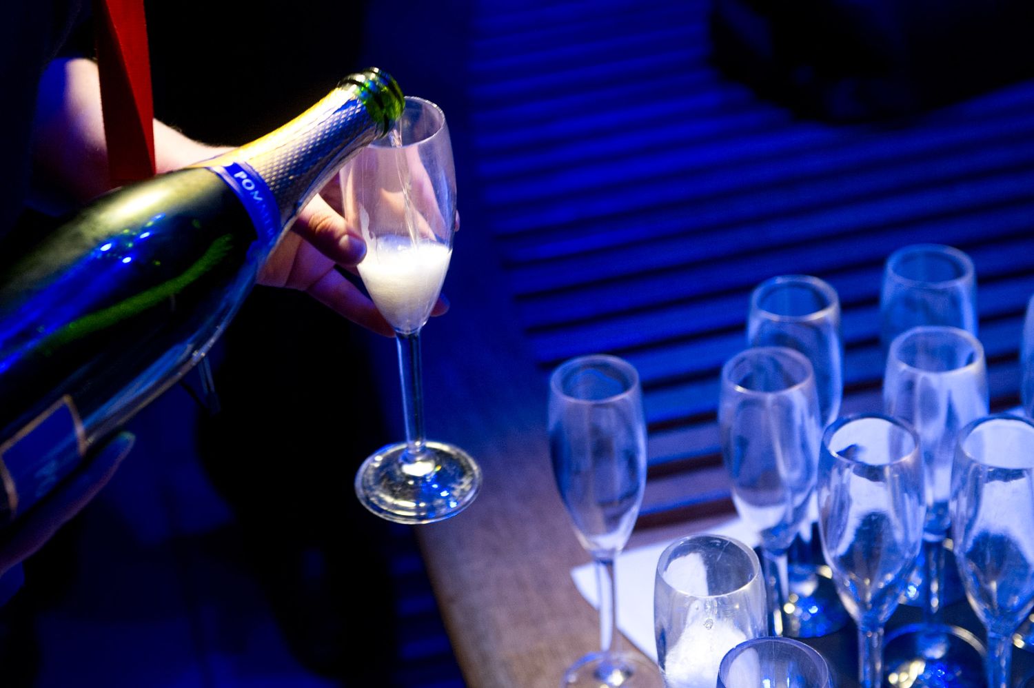 Wine glasses being filled with champagne in dramatic blue lighting at an event.