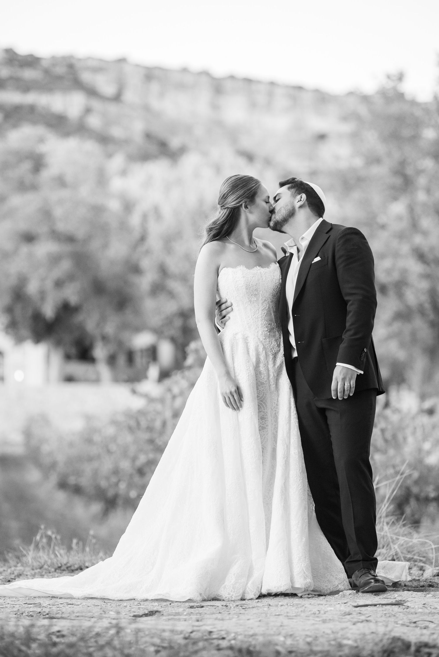 Black and white romantic wedding photo series showing couple in white dress and dark suit against scenic outdoor backdrop.
