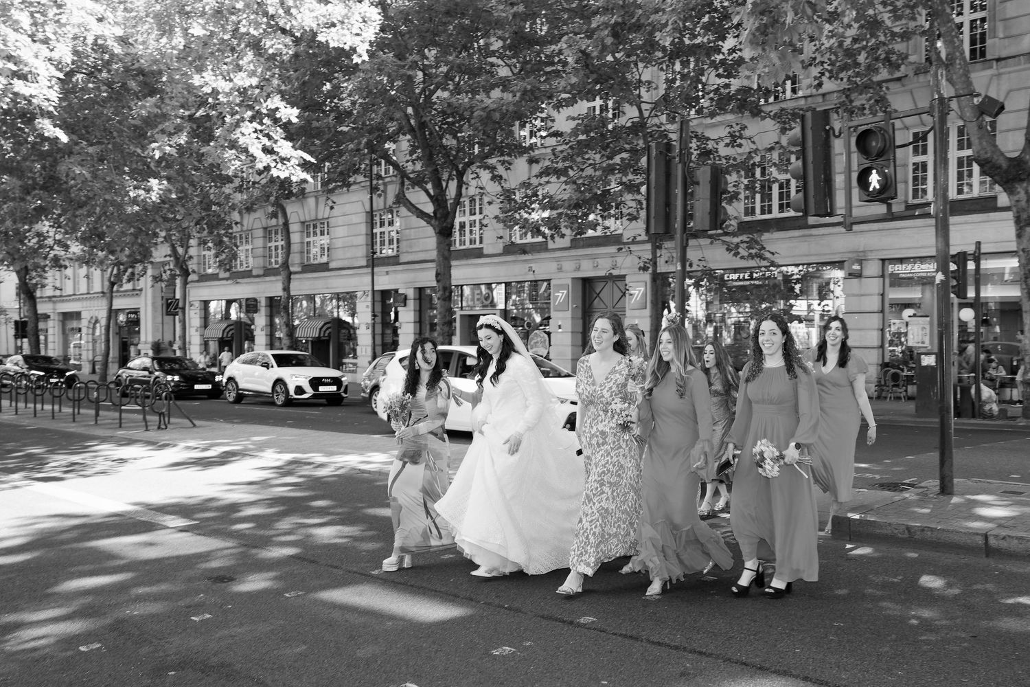 A vintage black and white photograph shows a wedding party walking down a tree-lined city street in the 1950s.
