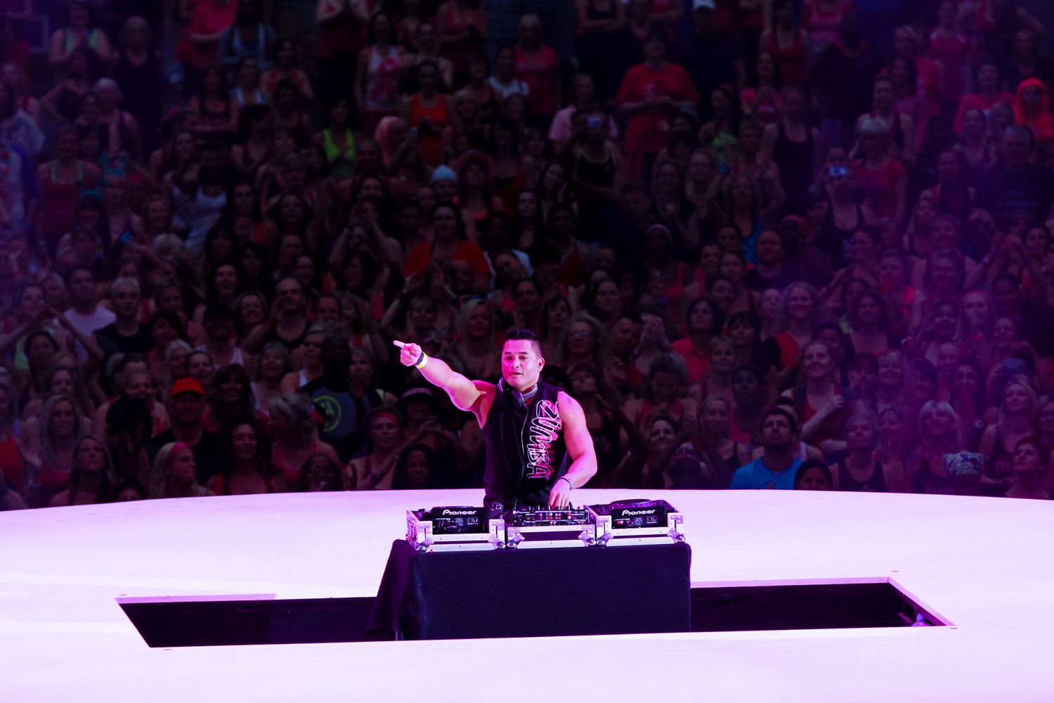 DJ performs at a nightclub event with colorful purple lighting and crowd in the background.