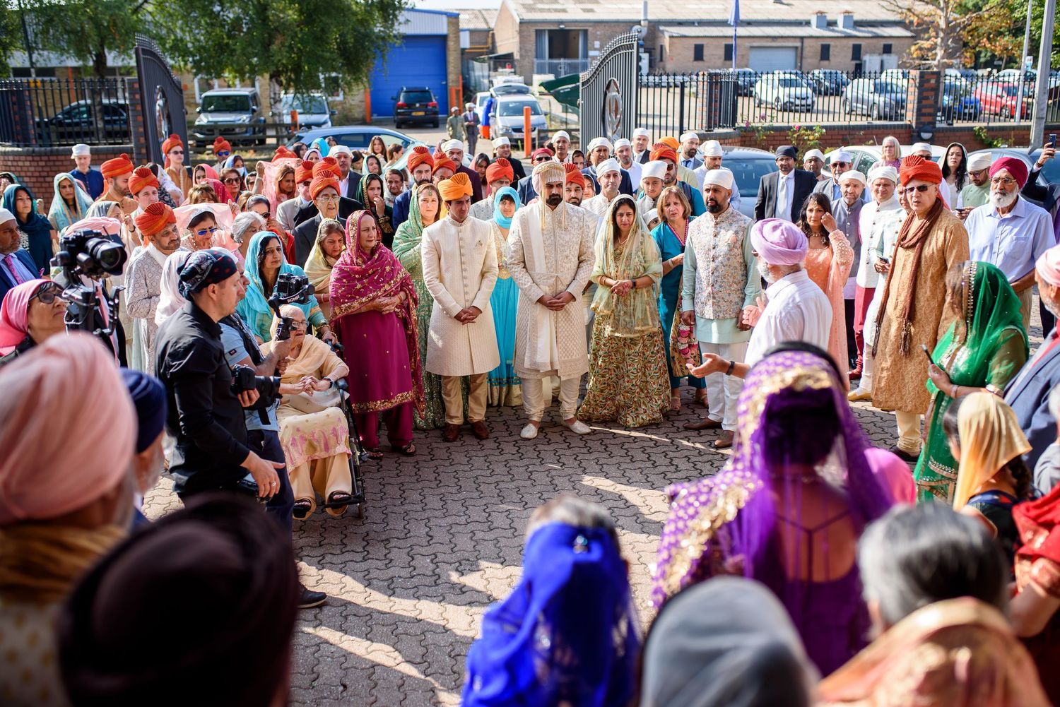 A large crowd of people wearing traditional colorful Indian attire gather outdoors for a cultural celebration.