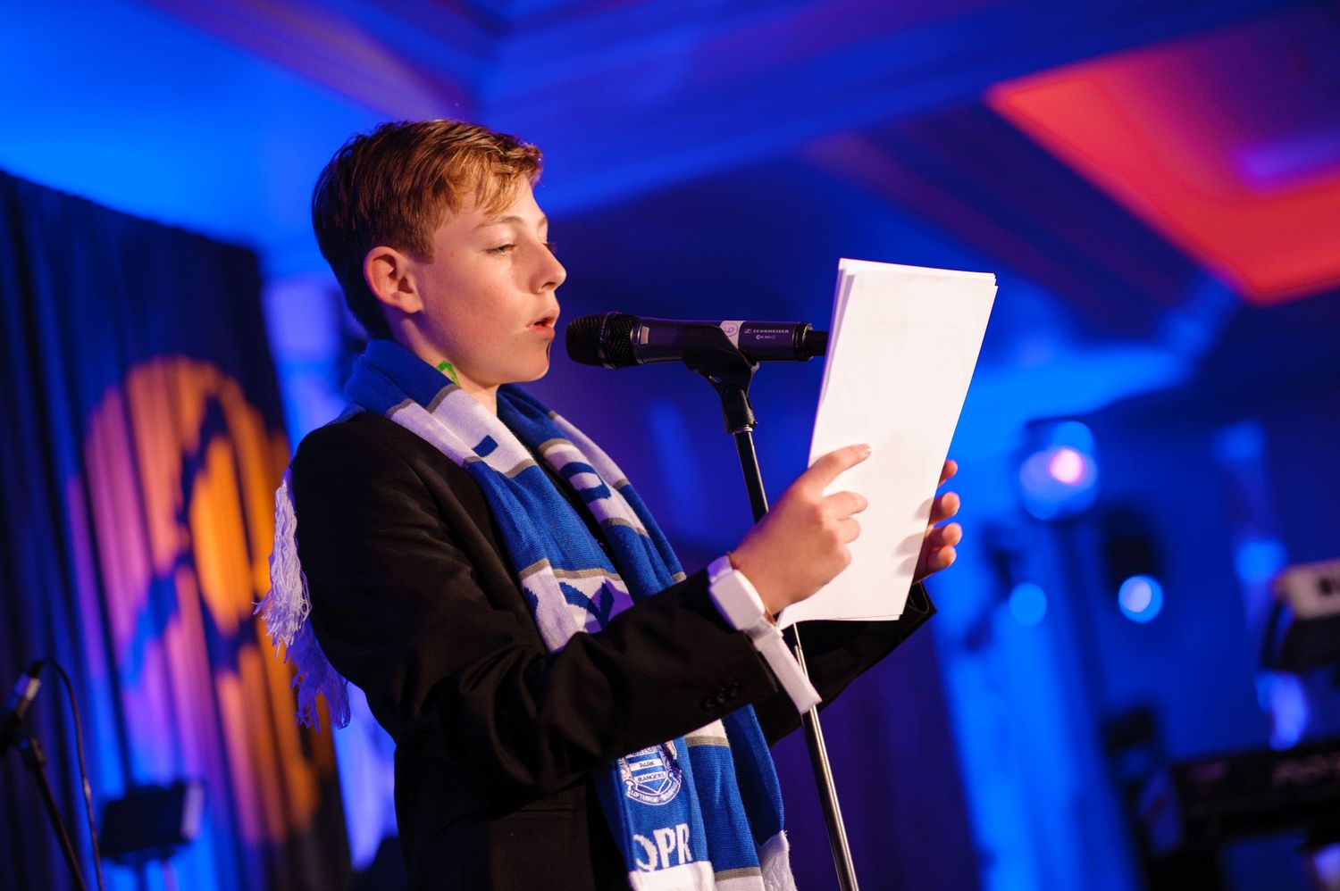 A person speaking at a podium in a room illuminated with blue and red lighting.