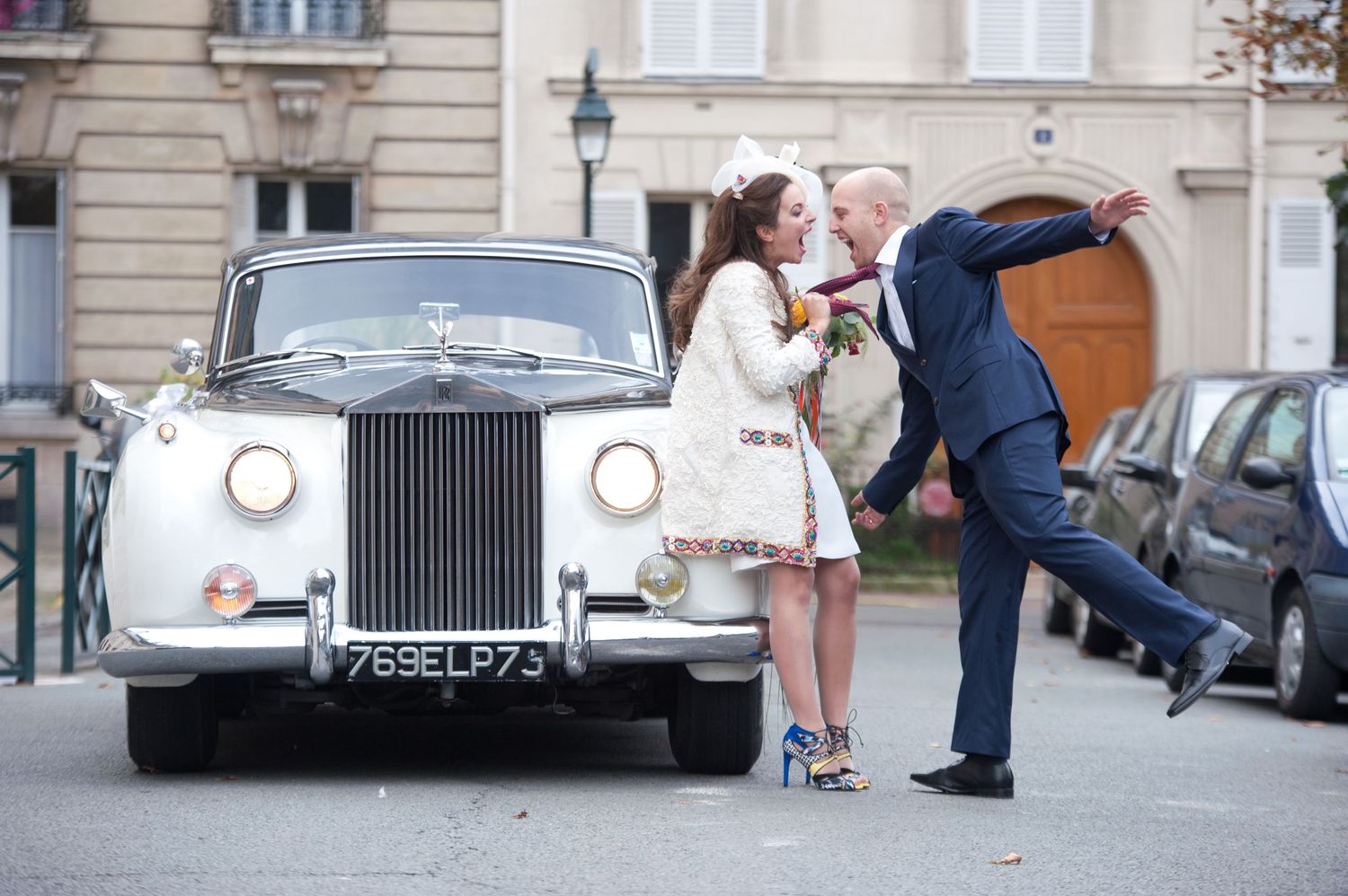 Couple posing romantically beside a classic white Rolls-Royce on a cobblestone street in Paris, France.