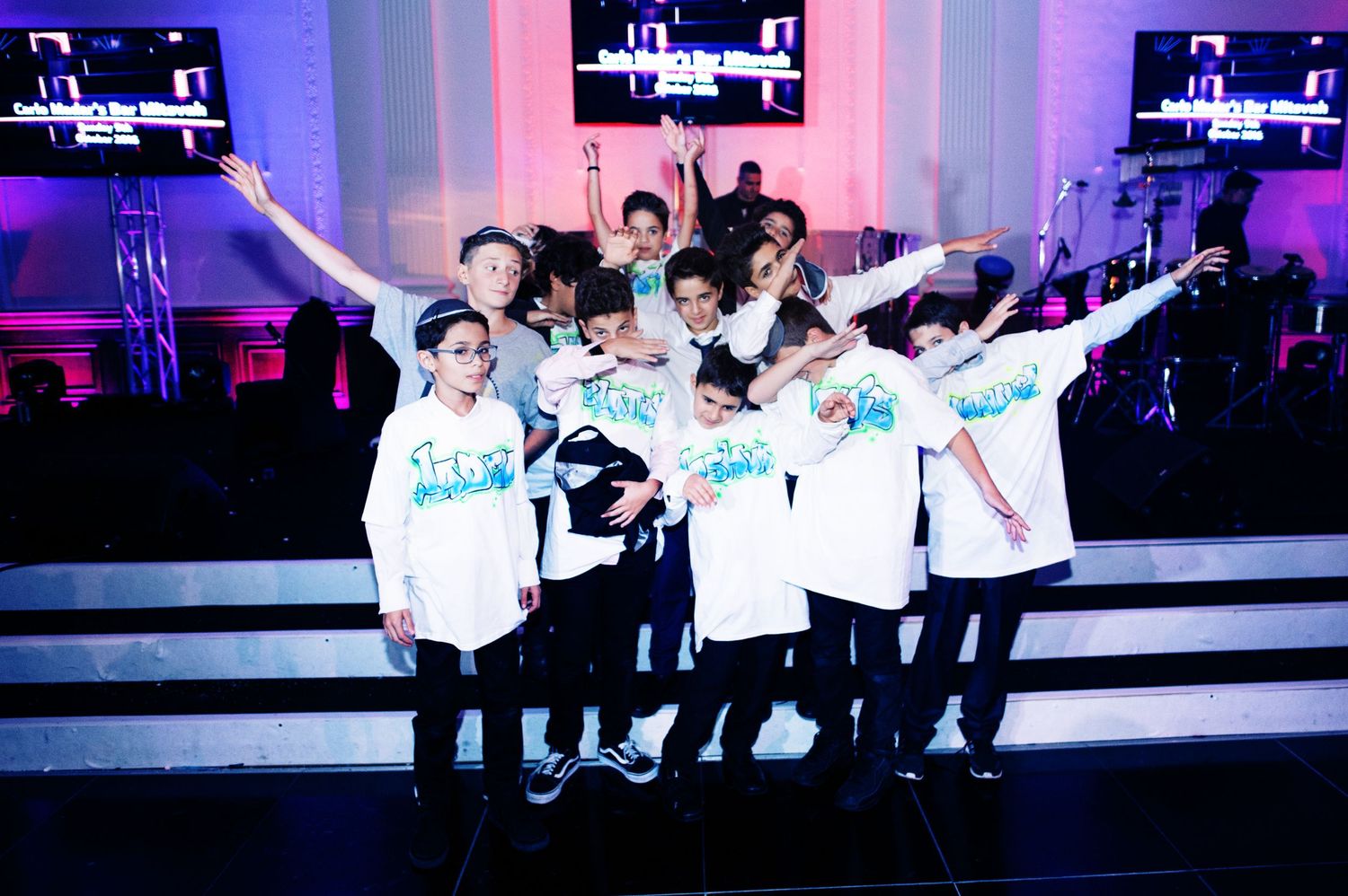 Performers in white outfits dance energetically on stage with blue and pink lighting effects creating a dynamic atmosphere.