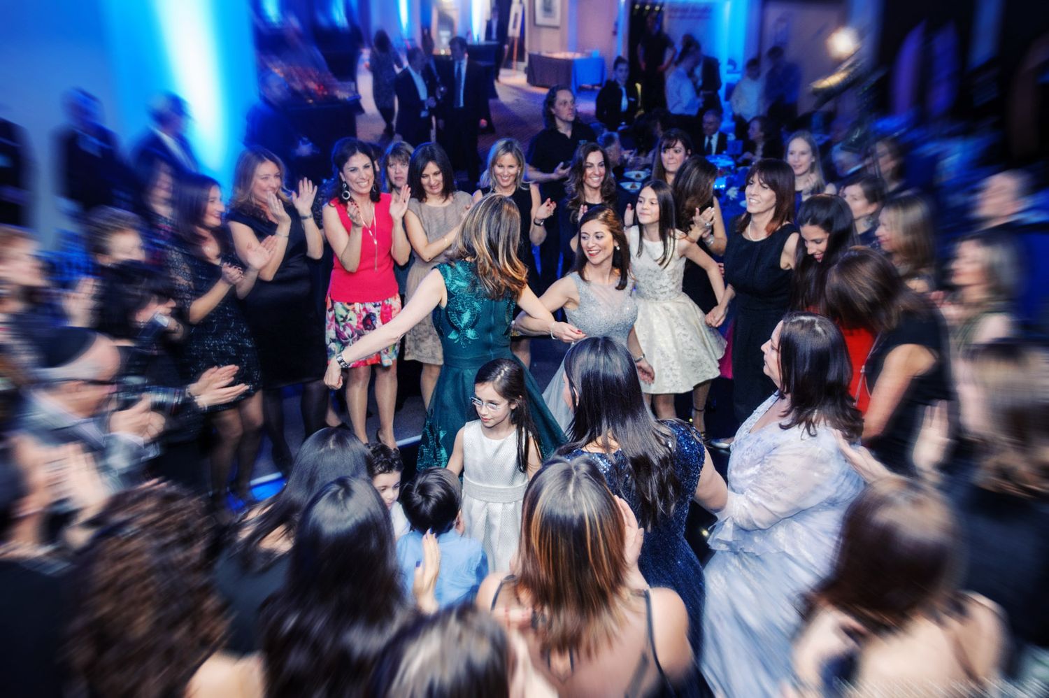 Energetic crowd dancing and moving at a nightclub with blue lighting and motion blur effects in the background.