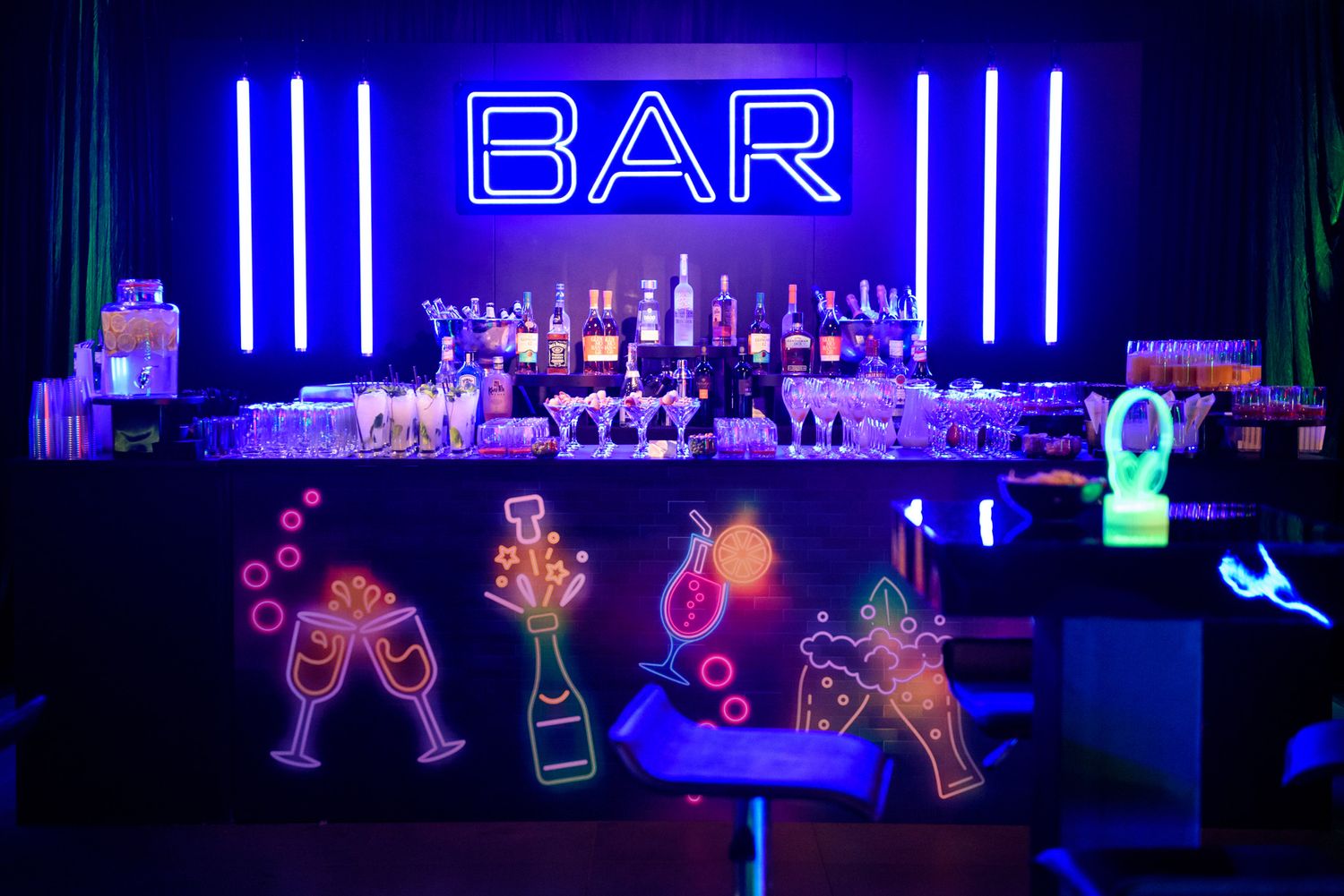 Neon blue bar signs and illuminated bottle decorations create a vibrant nightclub atmosphere.