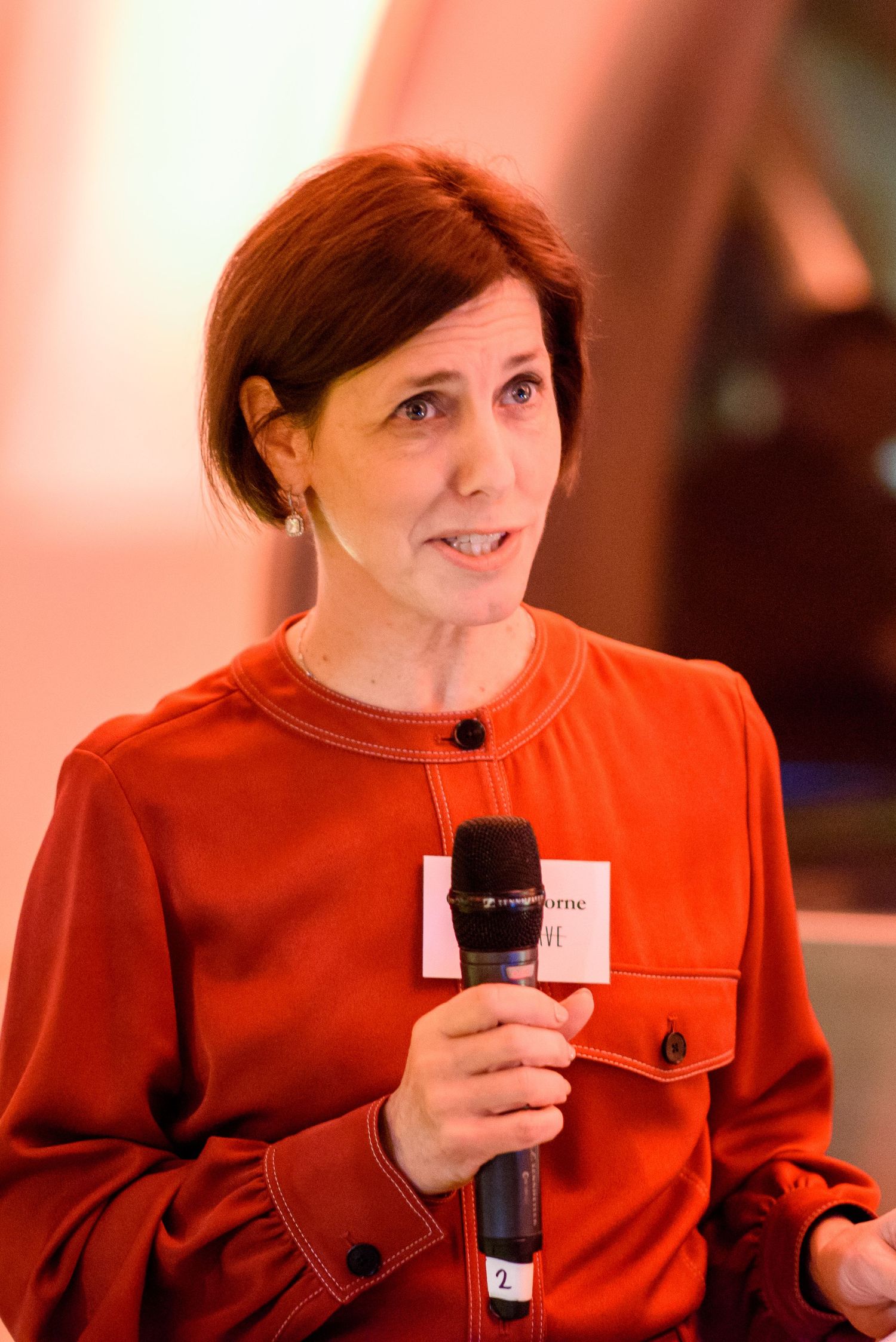 Speaker in bright red outfit presenting with microphone at professional event.