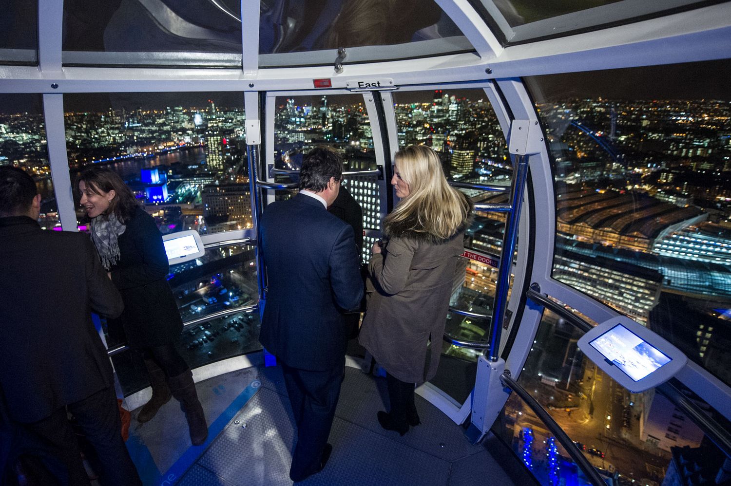 Visitors enjoying a nighttime city view from an observation deck with illuminated displays and screens.