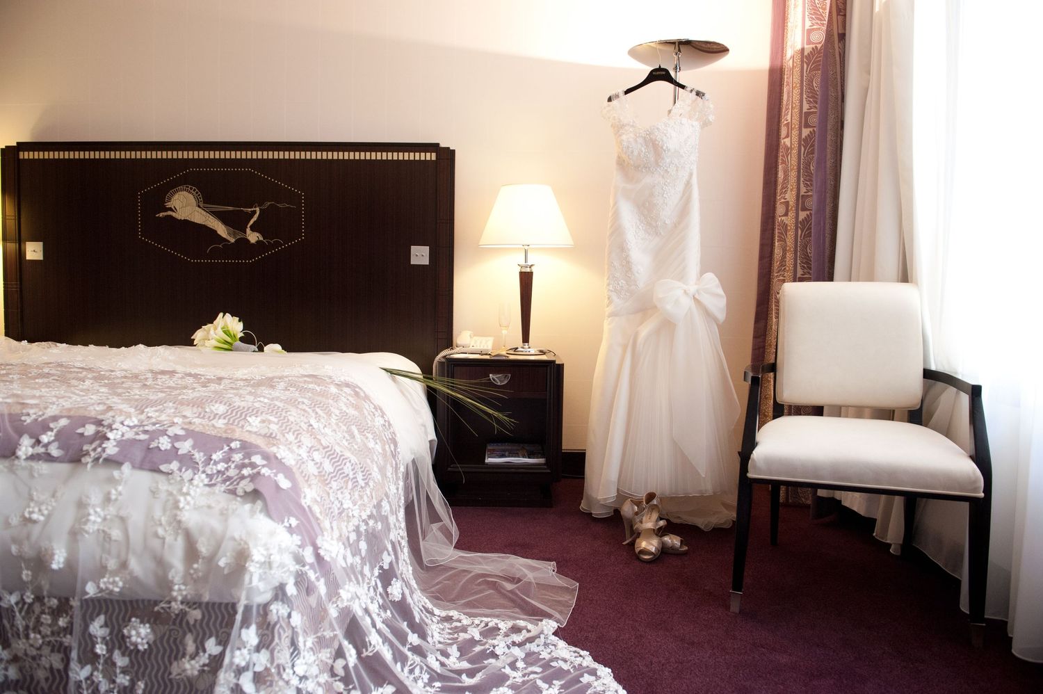 Elegant hotel room interior with burgundy carpet, white curtains, and modern furnishings in warm lighting.