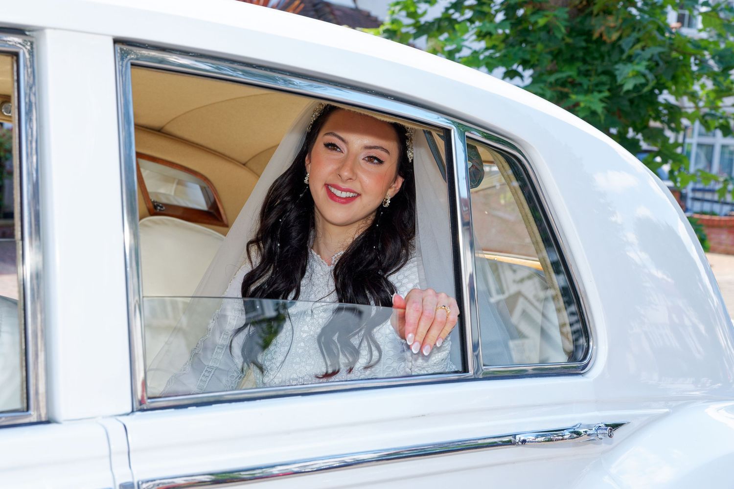 A passenger smiles and waves from the back window of a classic white vintage car.