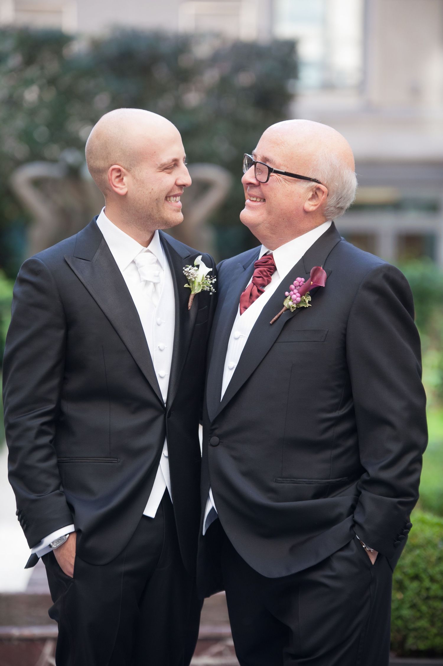 Two people in formal black suits and ties share an intimate moment during a wedding ceremony.