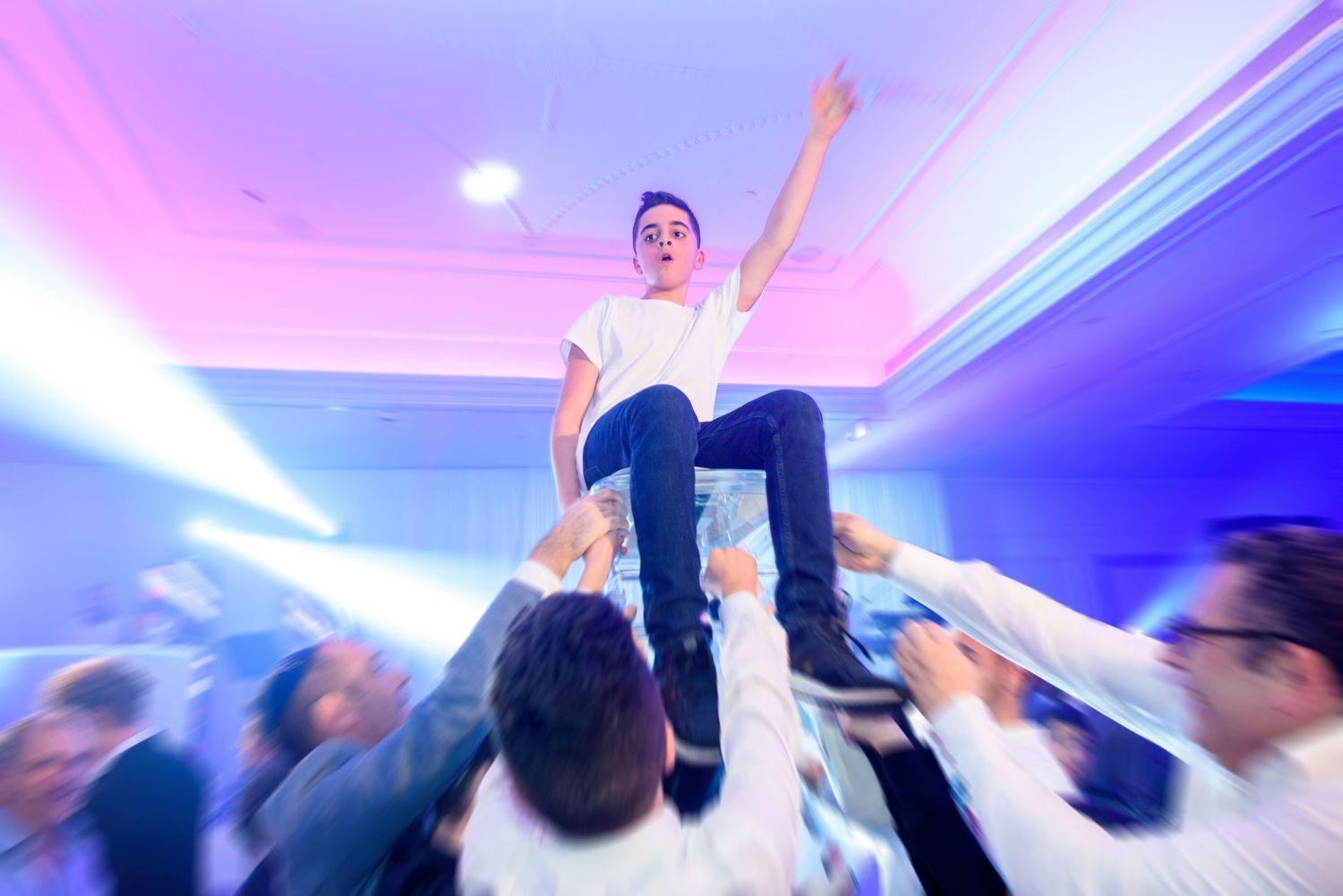 A crowd of people dancing and celebrating at a nightclub with colorful purple and pink lighting effects.