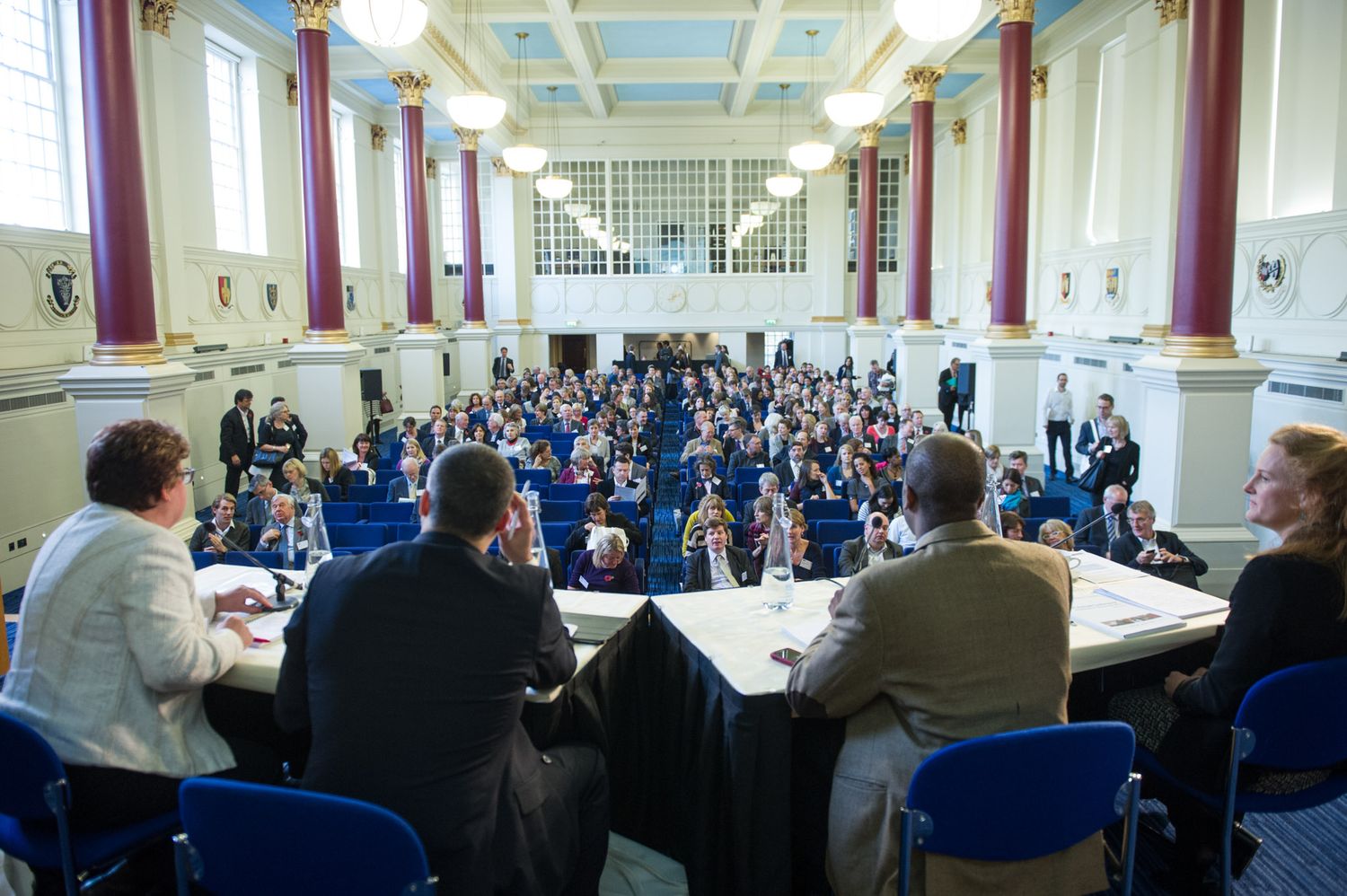Large conference room with long tables set up in rows and filled with attendees for a business meeting.