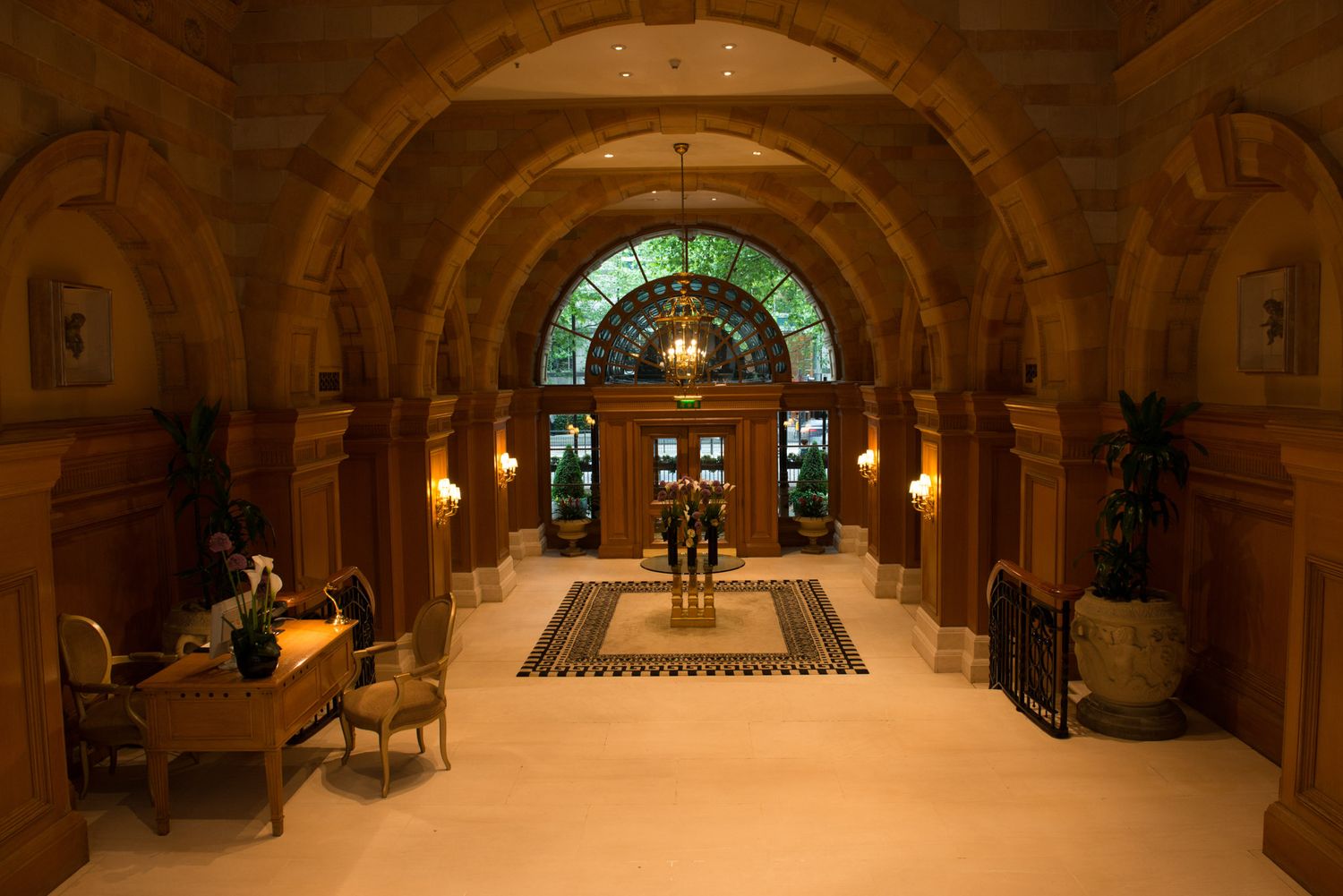 Elegant arched hallway with stained glass window and classic furniture in warm lighting.
