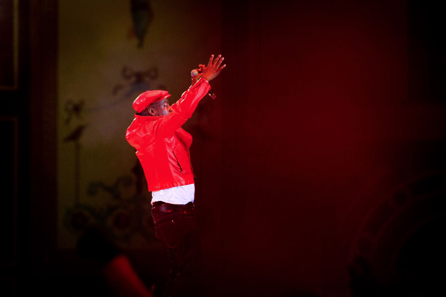 Performer in red illuminated by dramatic stage lighting during a show.
