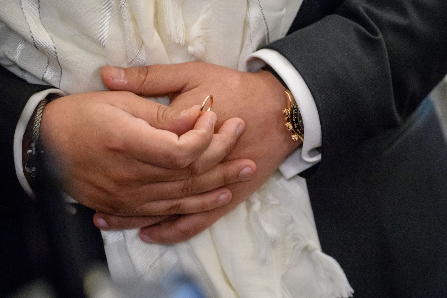 Close-up view of hands clasped together in formal attire showing white dress shirt and dark suit sleeves.