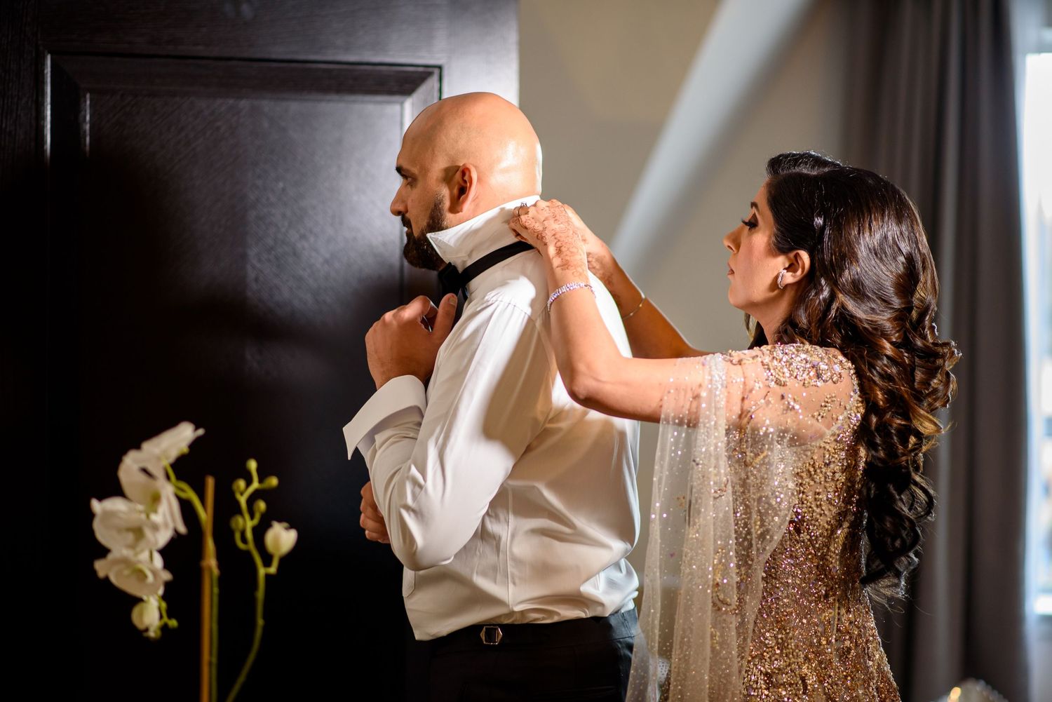 A bride in a sparkling sequin wedding dress holds a white bouquet while getting ready in a dark room.