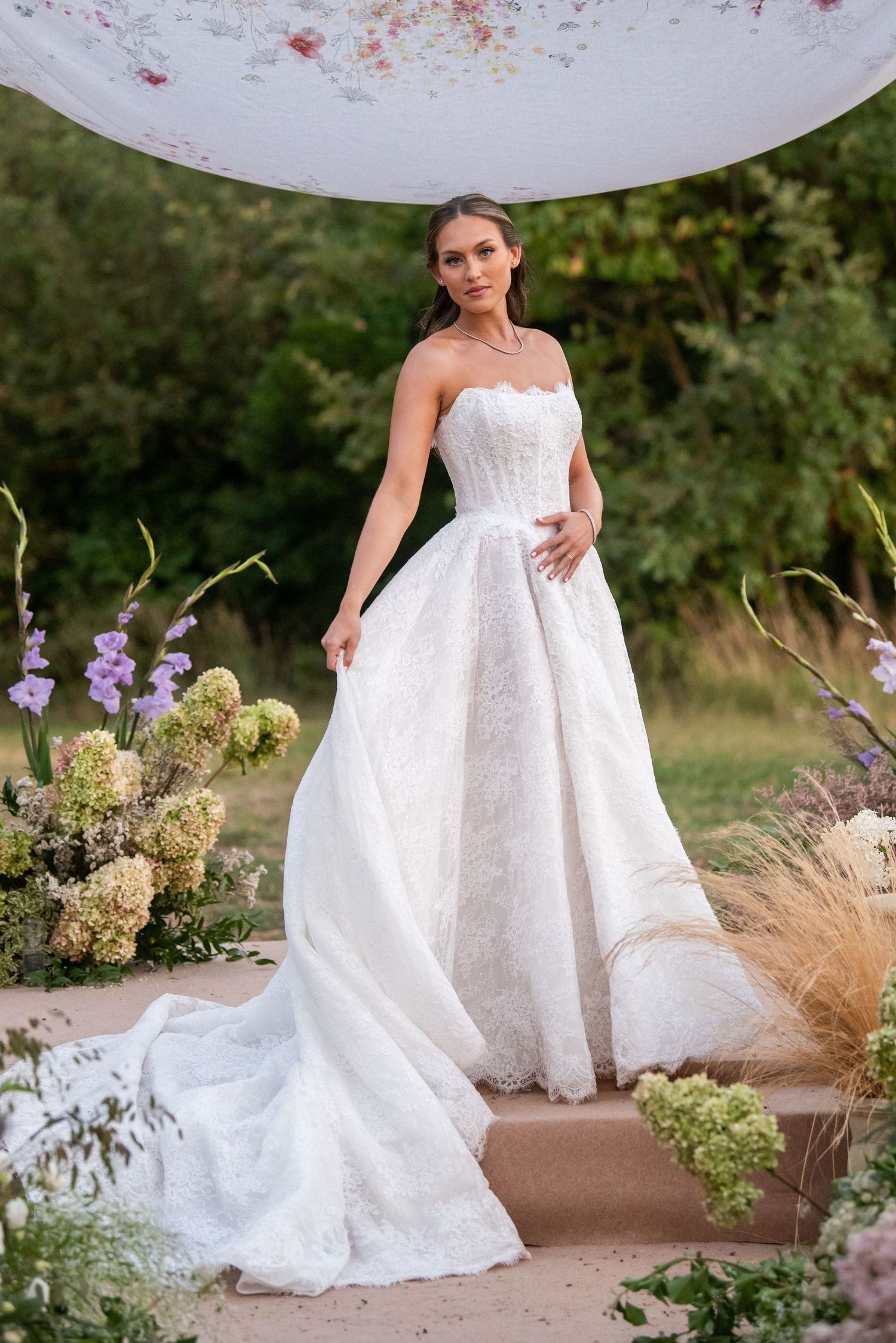 A stunning bridal portrait session in a garden setting featuring a flowing white lace wedding gown and natural floral elements.