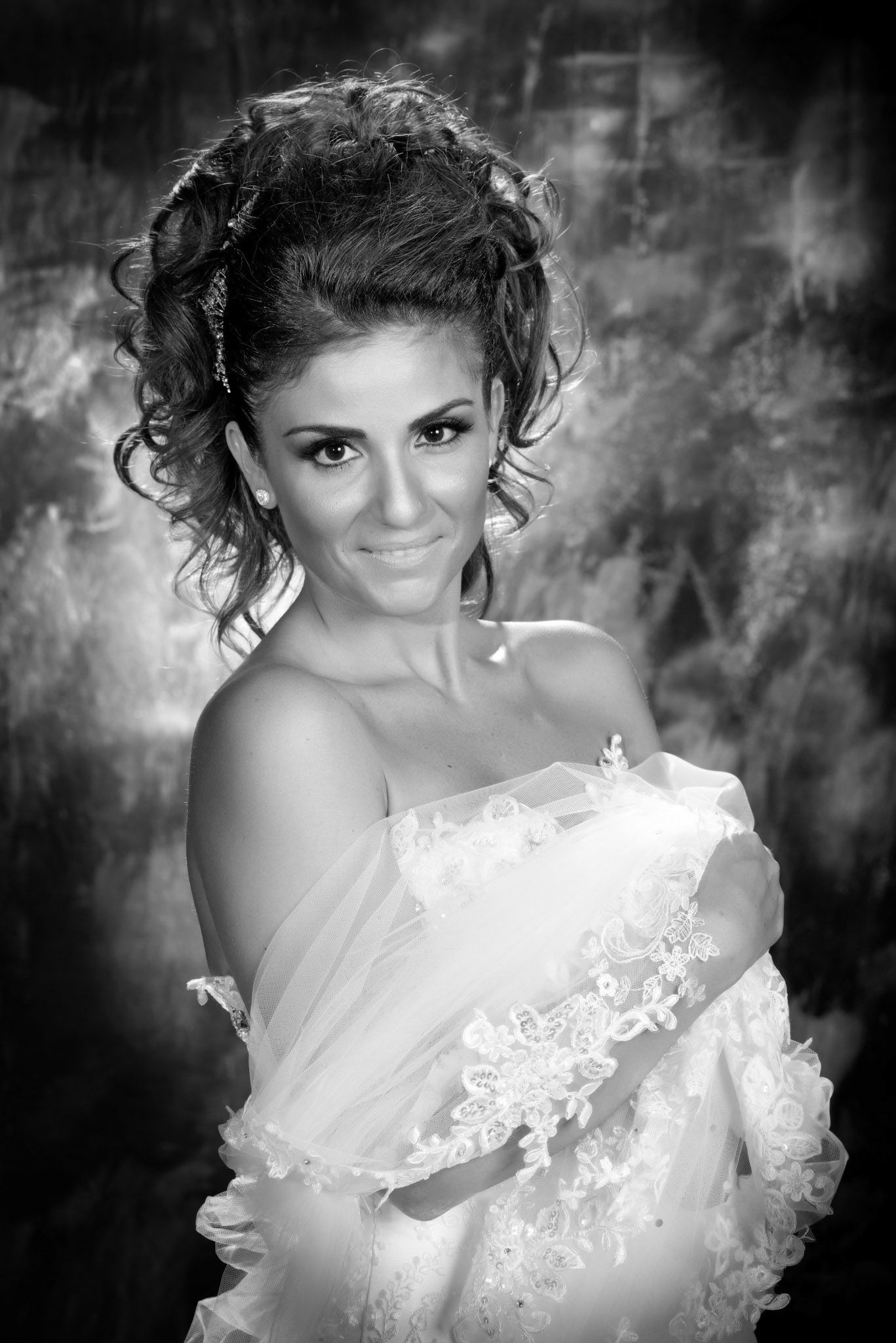Black and white portrait of a smiling bride in a lace wedding dress with an elegant updo hairstyle.