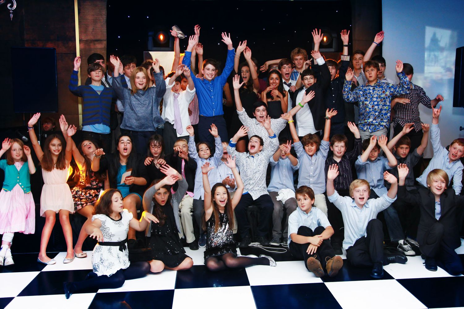 Large group of people dancing and celebrating at a nightclub or party venue with blue lighting effects.