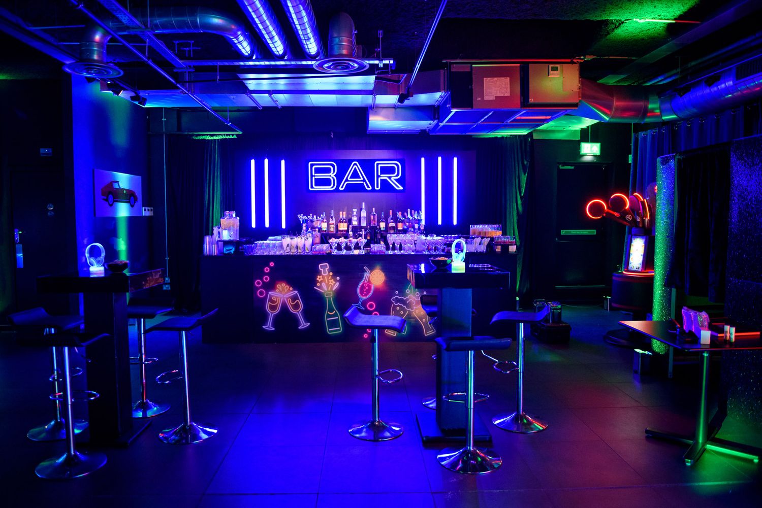 A dark nightclub interior illuminated by vibrant blue and green neon lights with a bar sign glowing in the background.