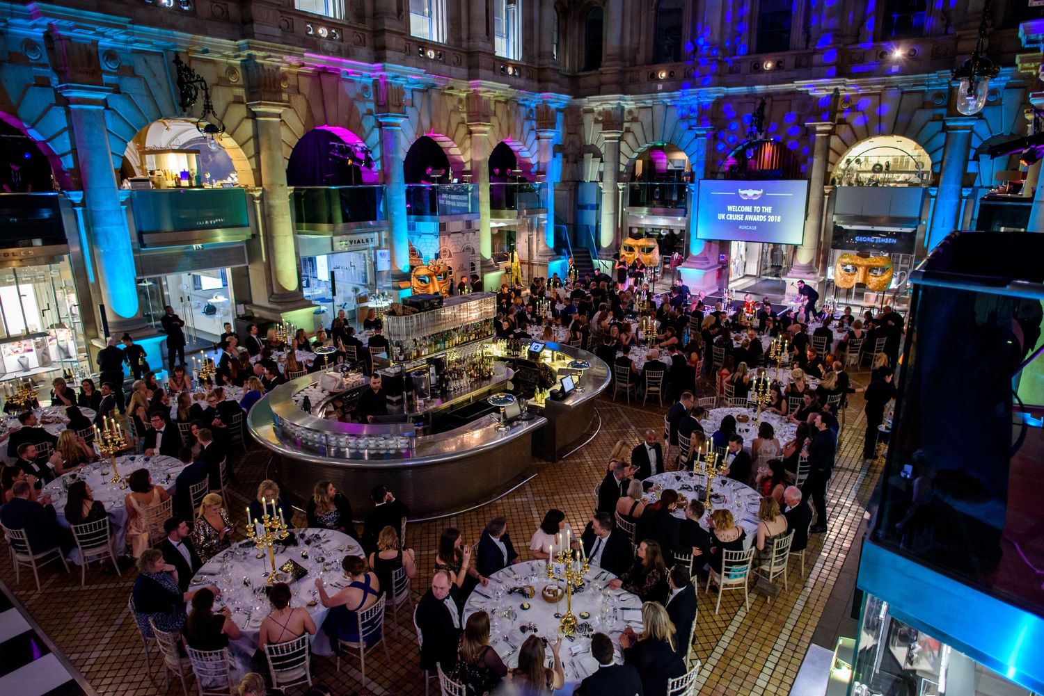 Elegant corporate dinner event with blue lighting and multiple round tables set for guests.