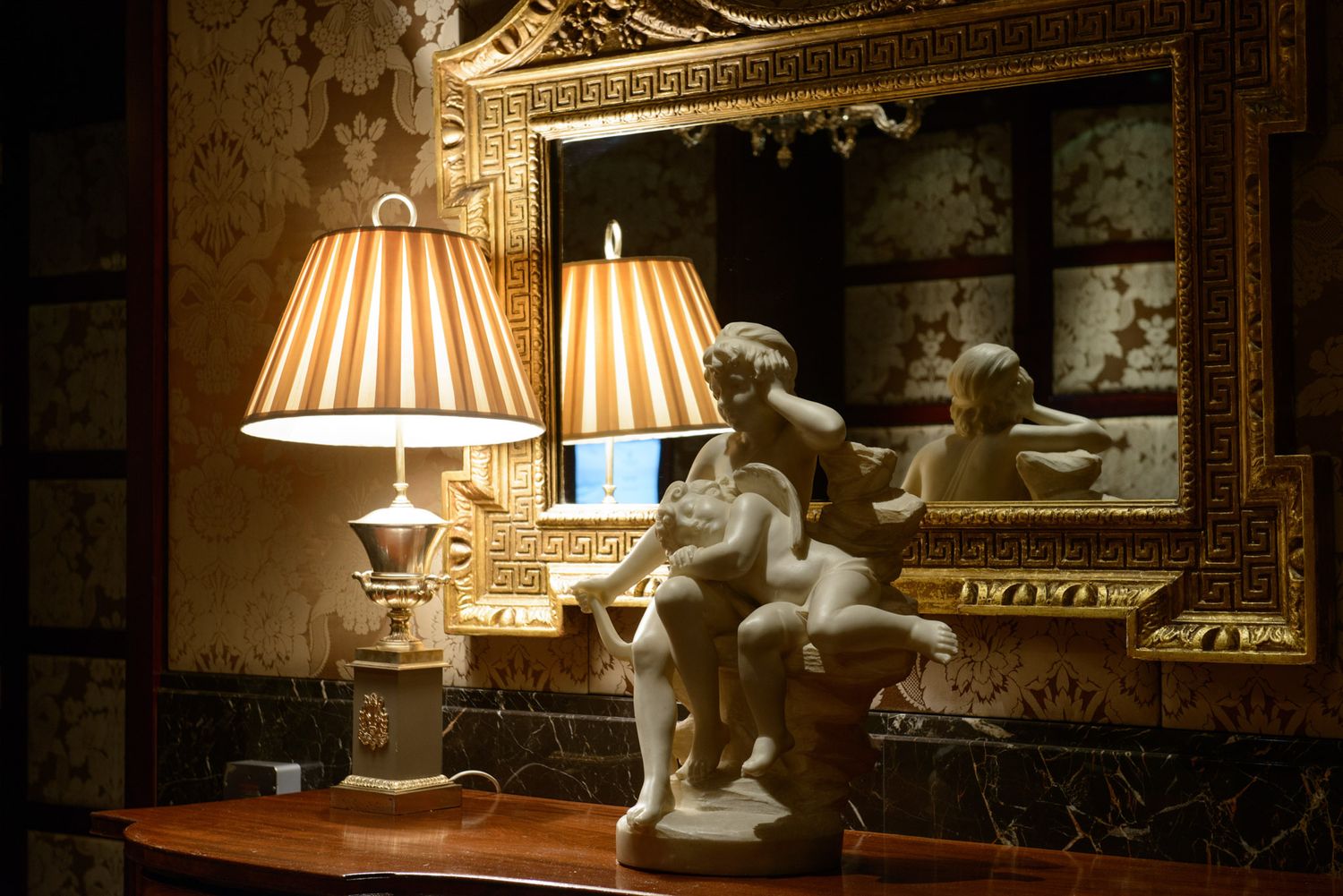 Elegant table lamp display with cherub statue and ornate gold mirror in a dimly lit luxurious setting.