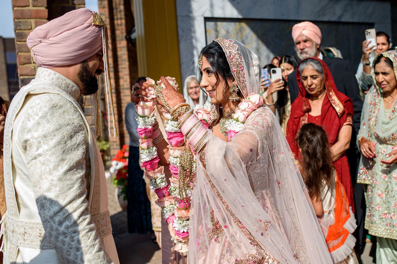 Joyful wedding celebration with guests throwing flower petals at a traditional Indian ceremony outside a brick building.