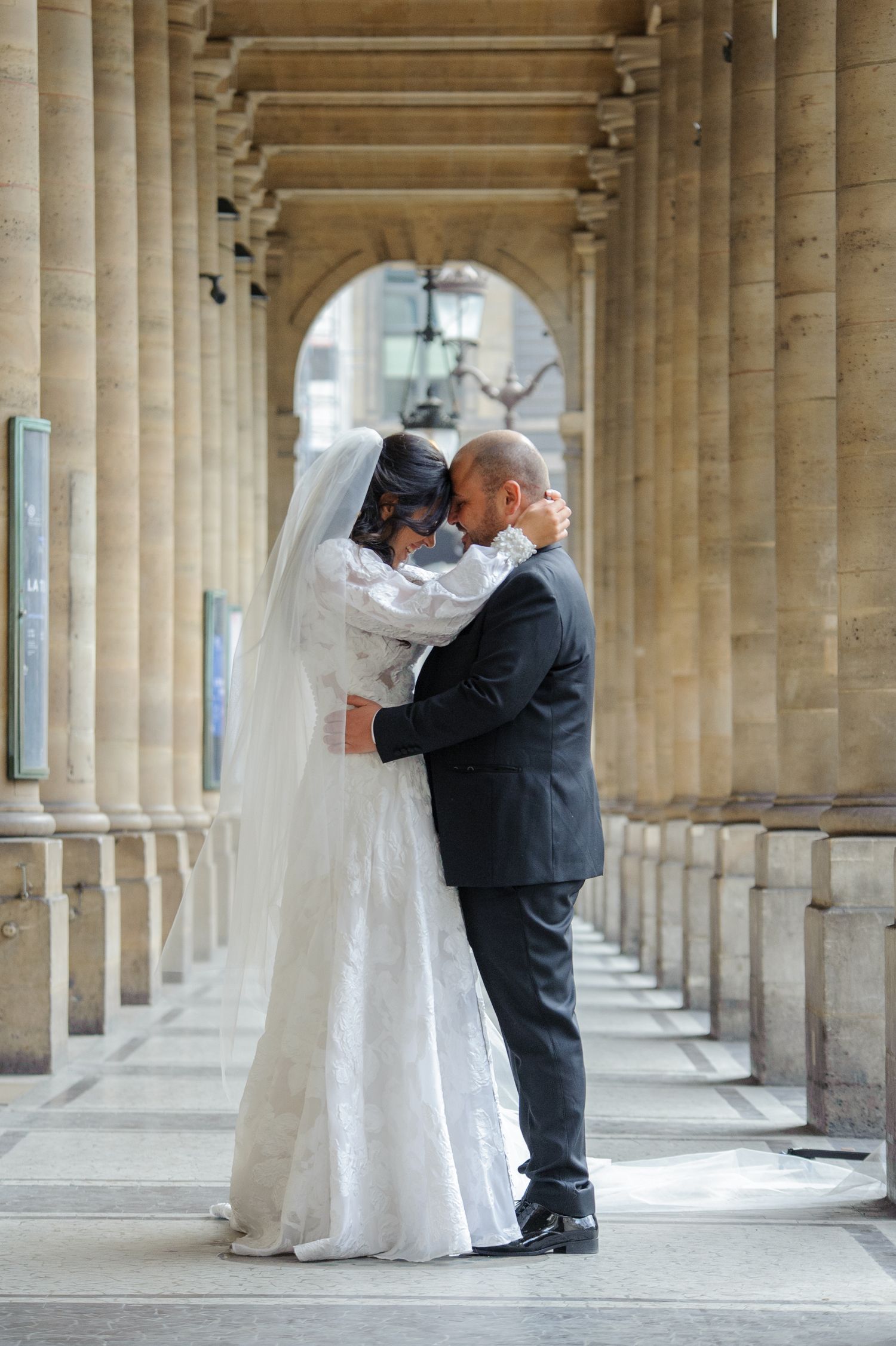 A romantic wedding photo sequence captured under an elegant colonnade with classical stone pillars and arches.
