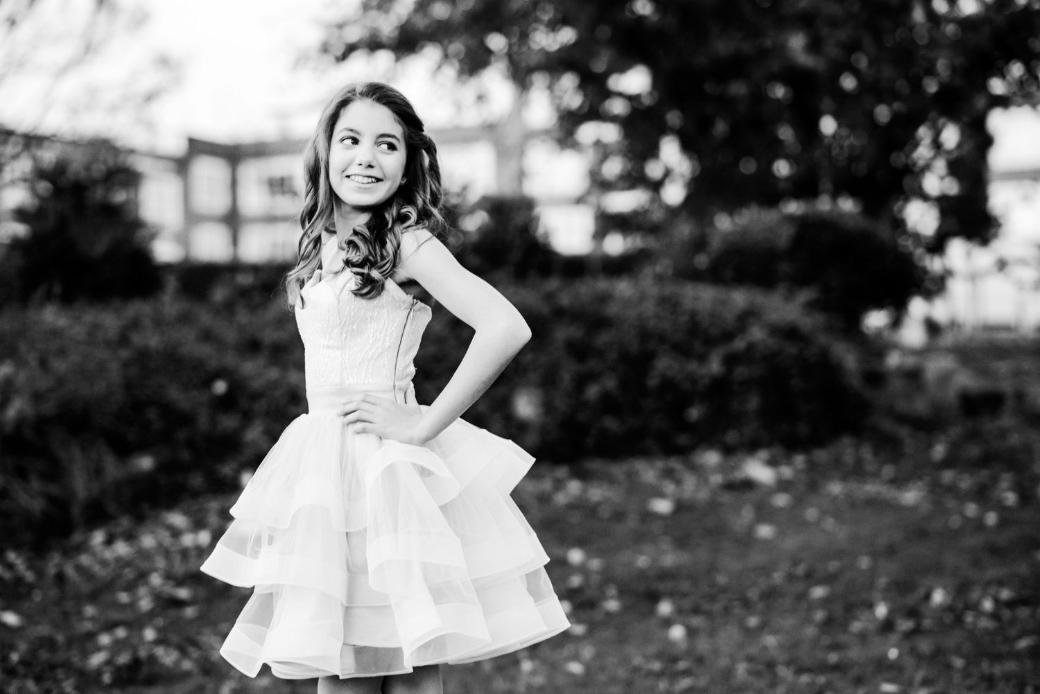 A child in a white dress twirls playfully in a garden setting on a sunny day.