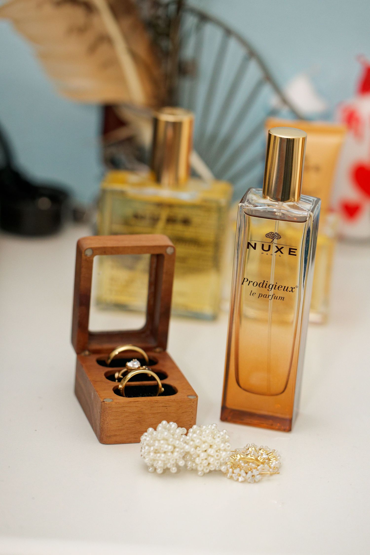 Luxury perfume bottles and pearl jewelry displayed on white surface with soft blue background.