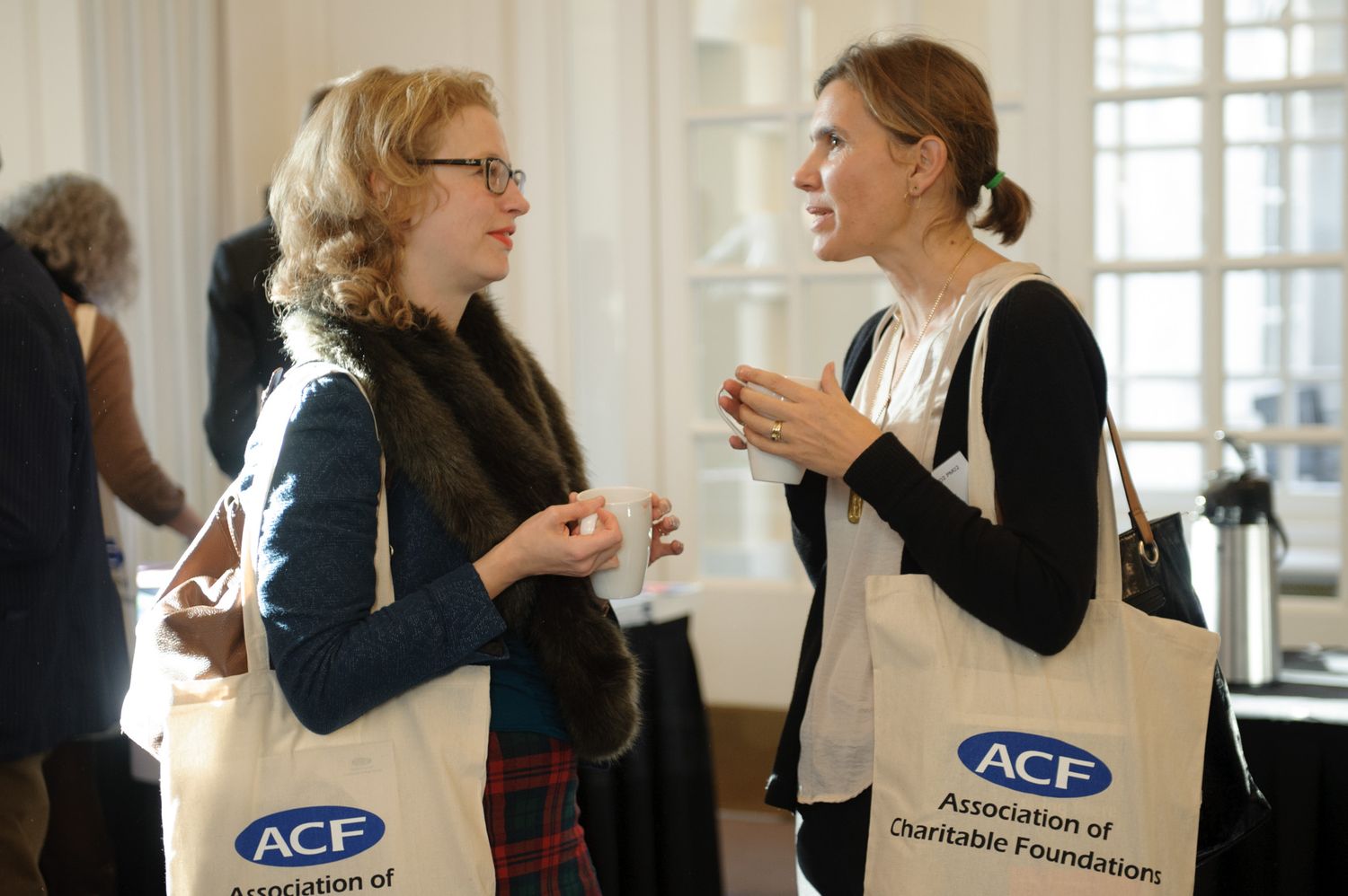 Two conference attendees with ACF tote bags engaged in conversation during a networking break.