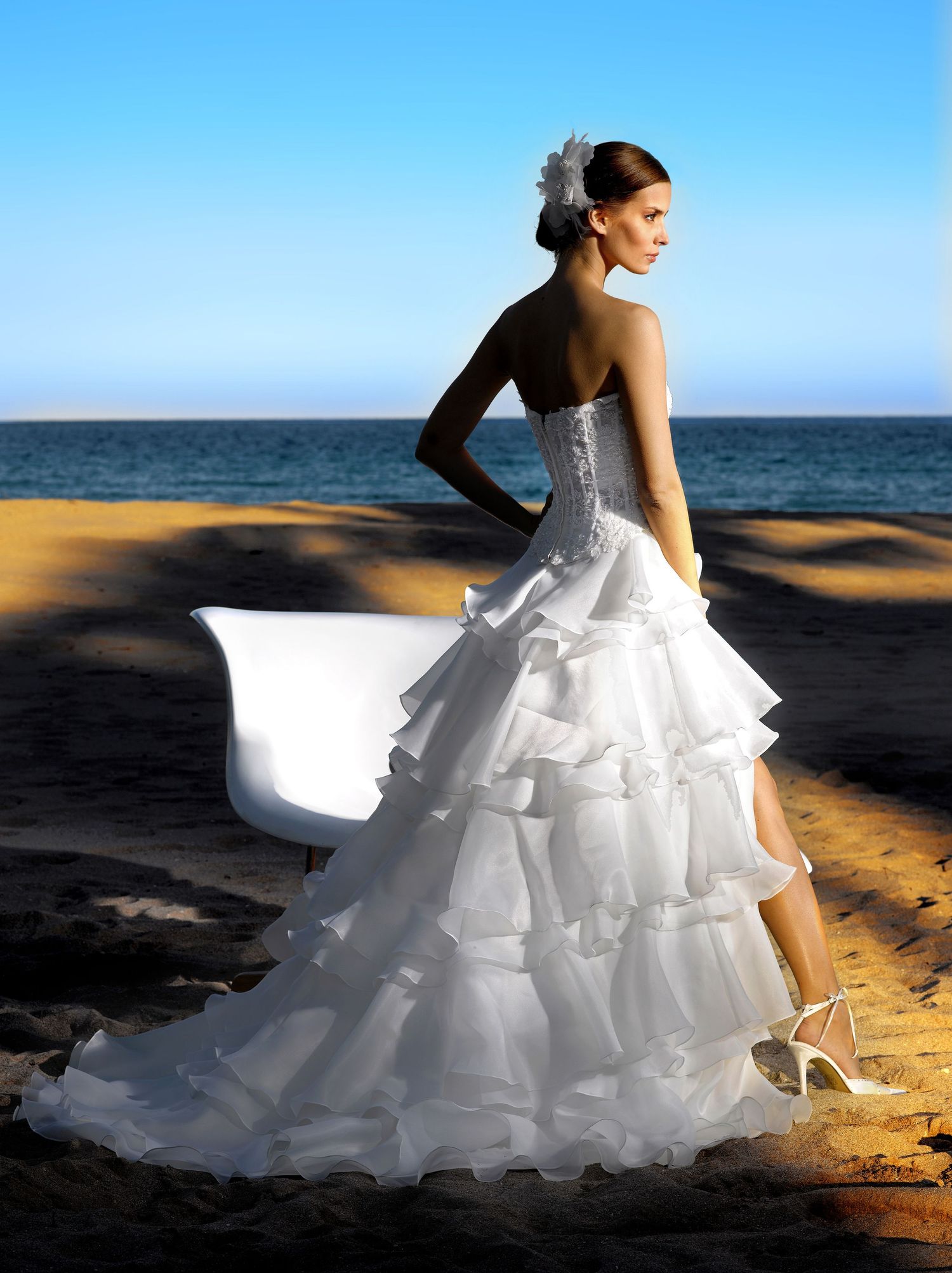 Bride in white ruffled strapless wedding gown with train poses on sandy beach with ocean backdrop.