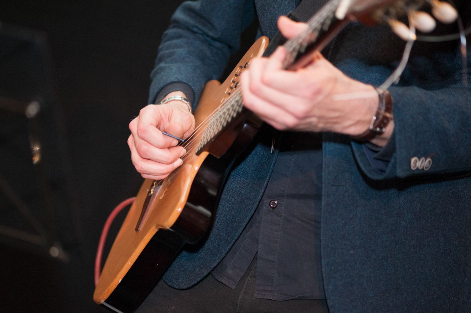 Musicians hands playing acoustic guitar in dark concert setting.