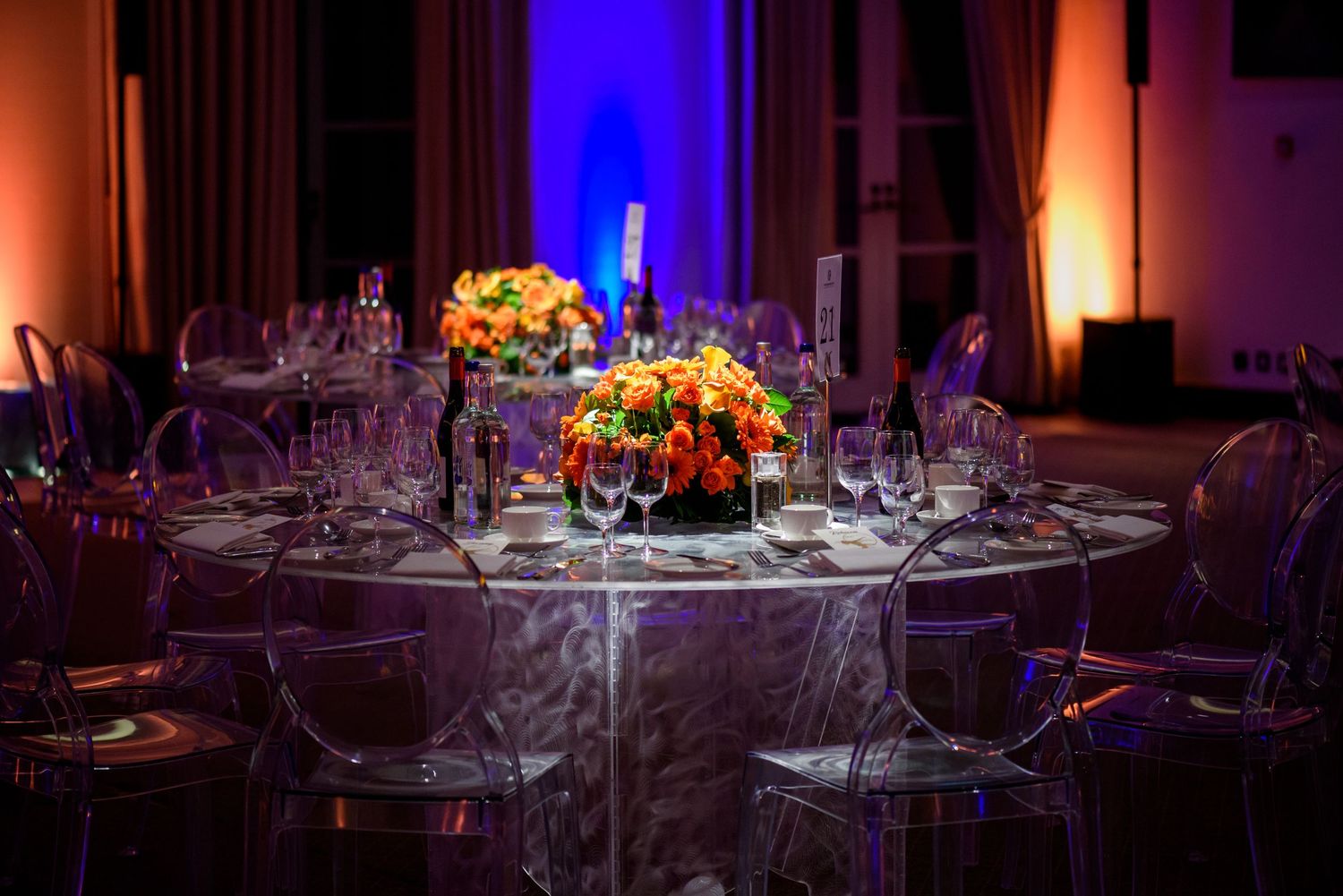 Elegant banquet hall setup with round tables and dramatic purple and orange lighting.