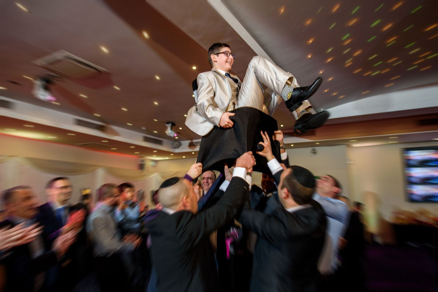 People dance and celebrate at a lively party with colorful disco lights illuminating the dance floor.