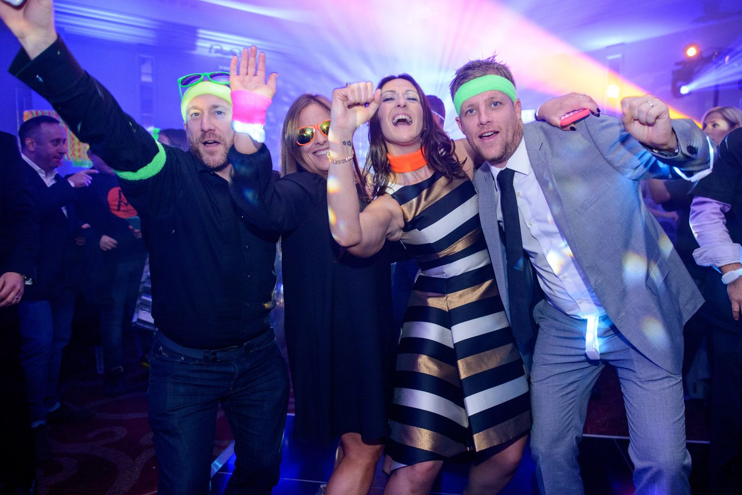 People dancing and celebrating at a nightclub party with blue lighting and neon accessories.