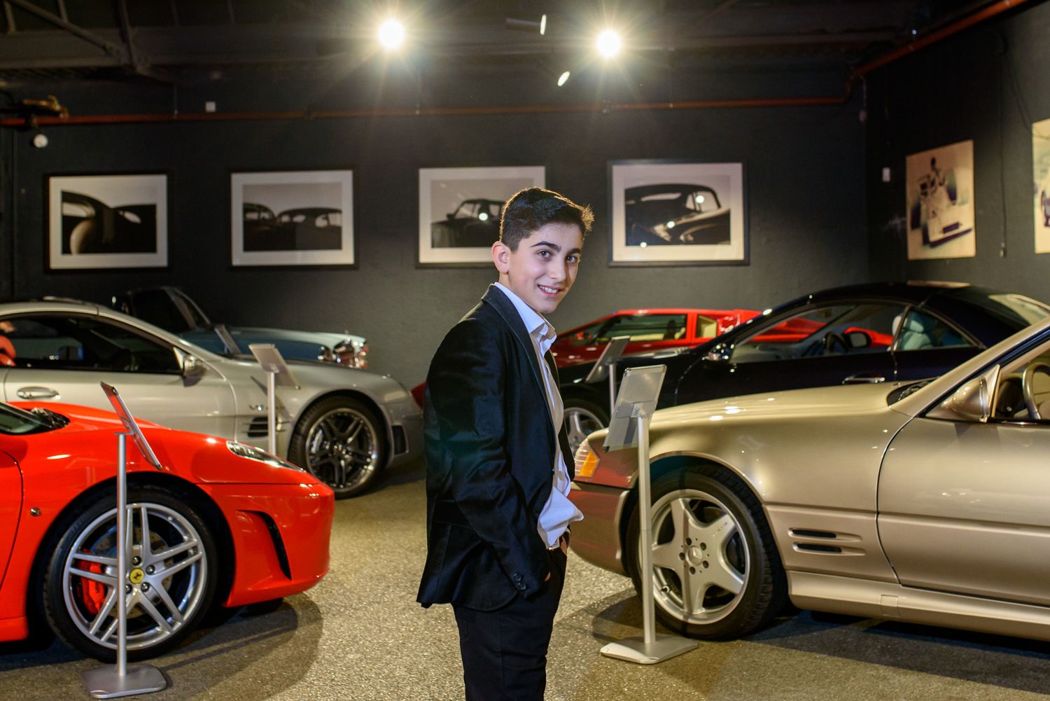 A luxury car showroom displays multiple high-end vehicles under dramatic lighting with framed artwork on the walls.