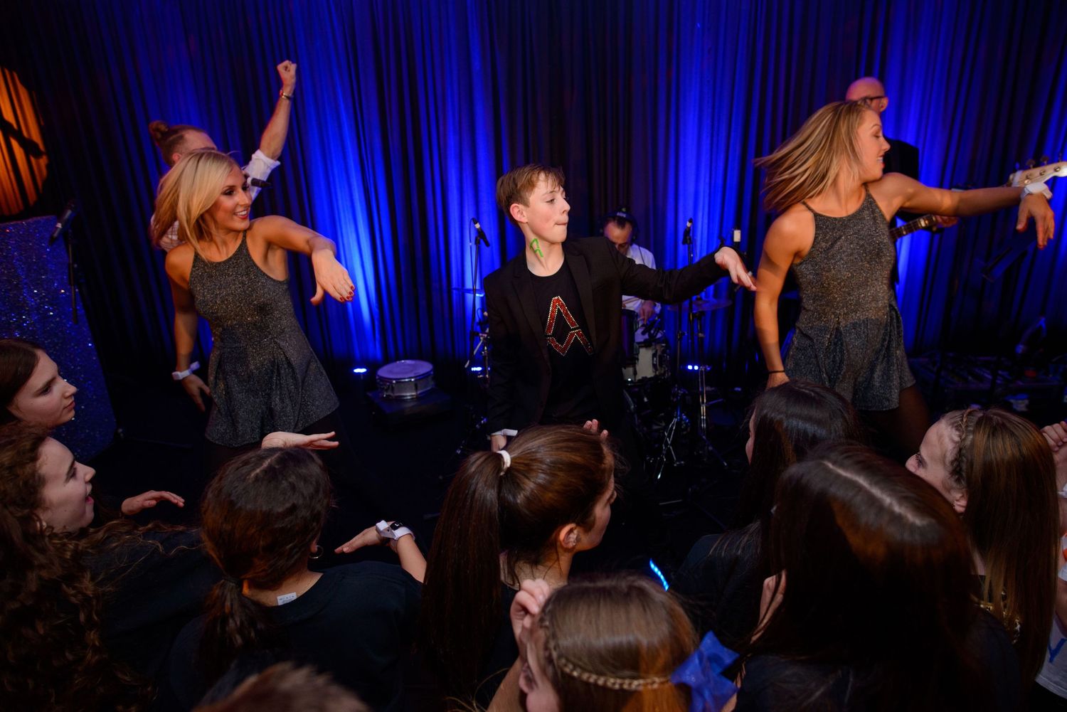 Dancers in black outfits perform a dynamic contemporary dance routine on stage under dramatic blue lighting.