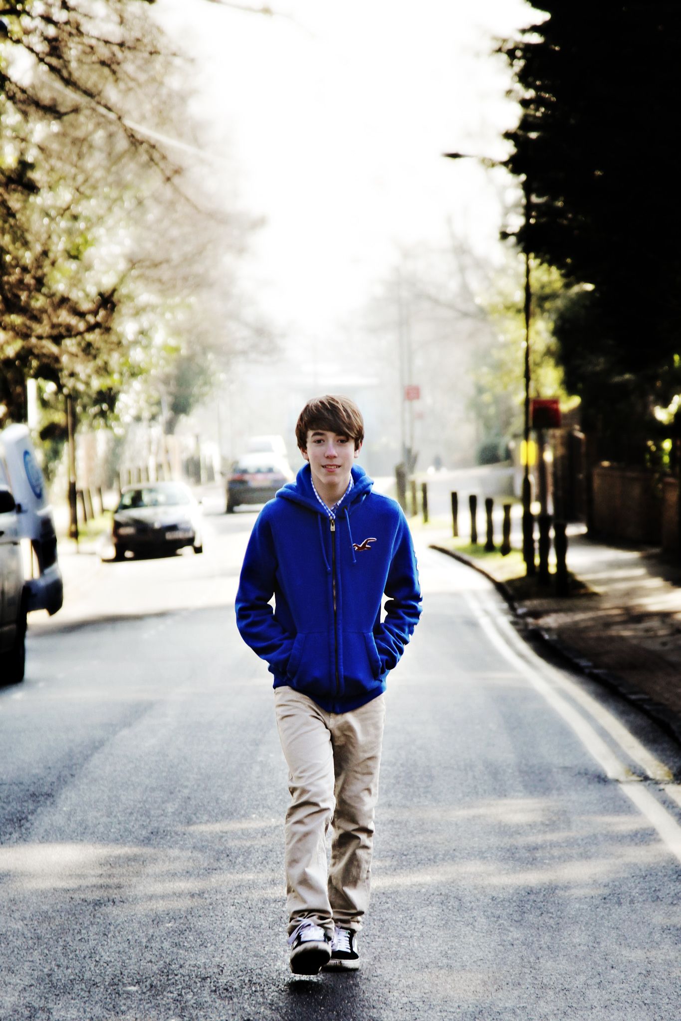 A person in a blue hoodie and khaki pants walks down a misty tree-lined street.